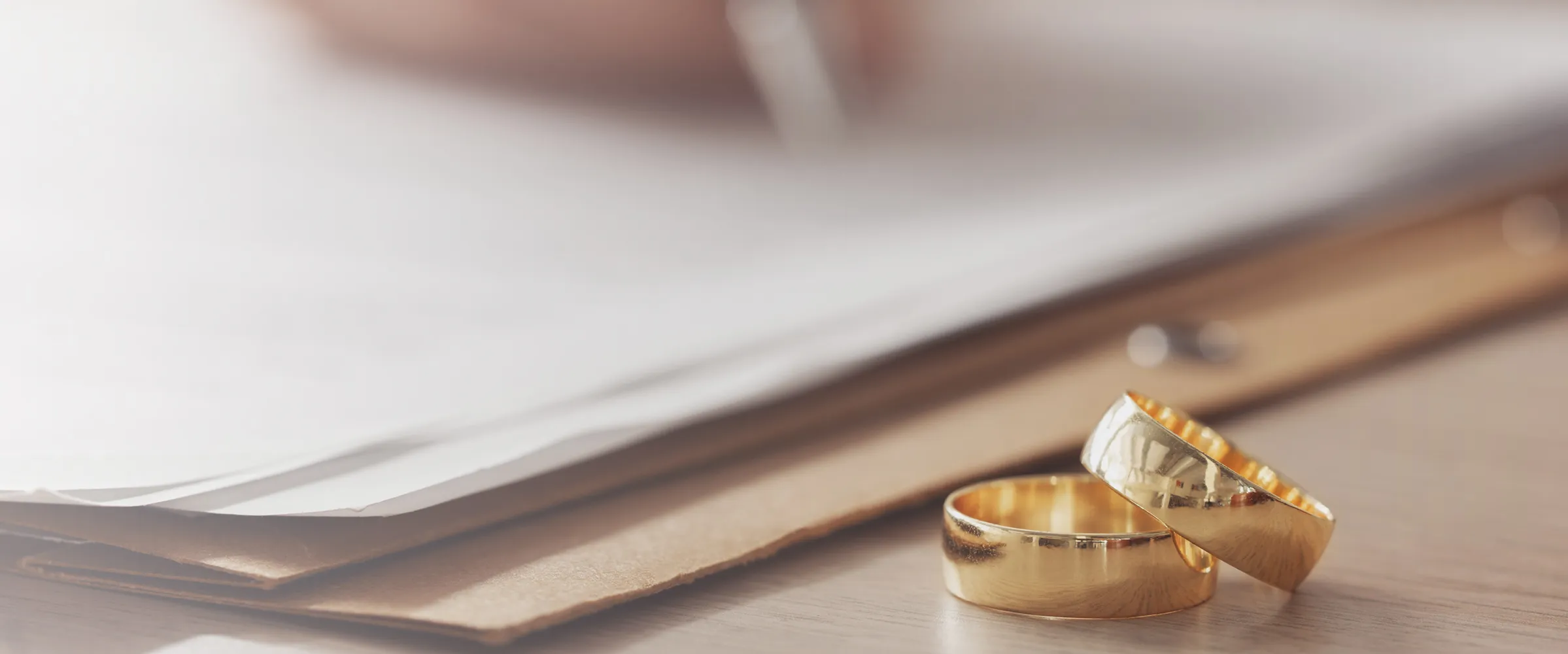 Two gold wedding rings on a table with paperwork in the background.