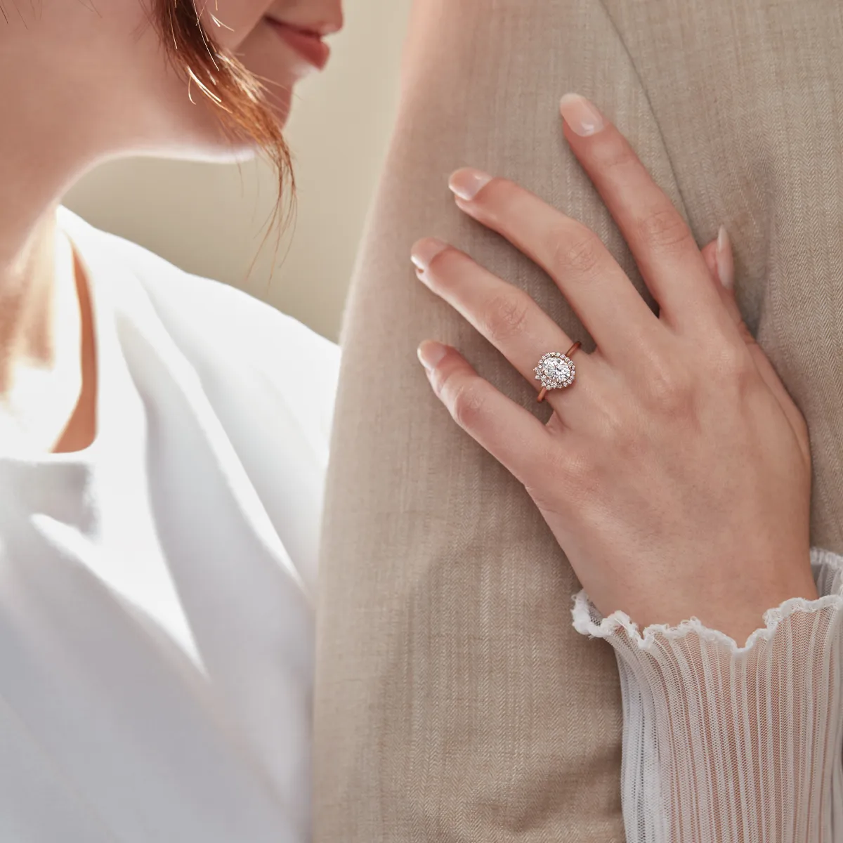A woman shows off her engagement ring while leaning against a man's arm, highlighting the ring's sparkle.