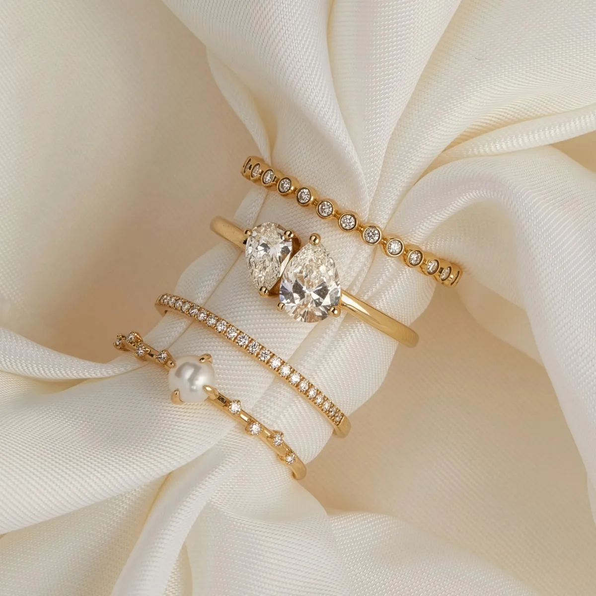 Four elegant gold rings with diamonds and a pearl, displayed on soft cream fabric. Shop at Golden Gifts Jewelry in Milford.