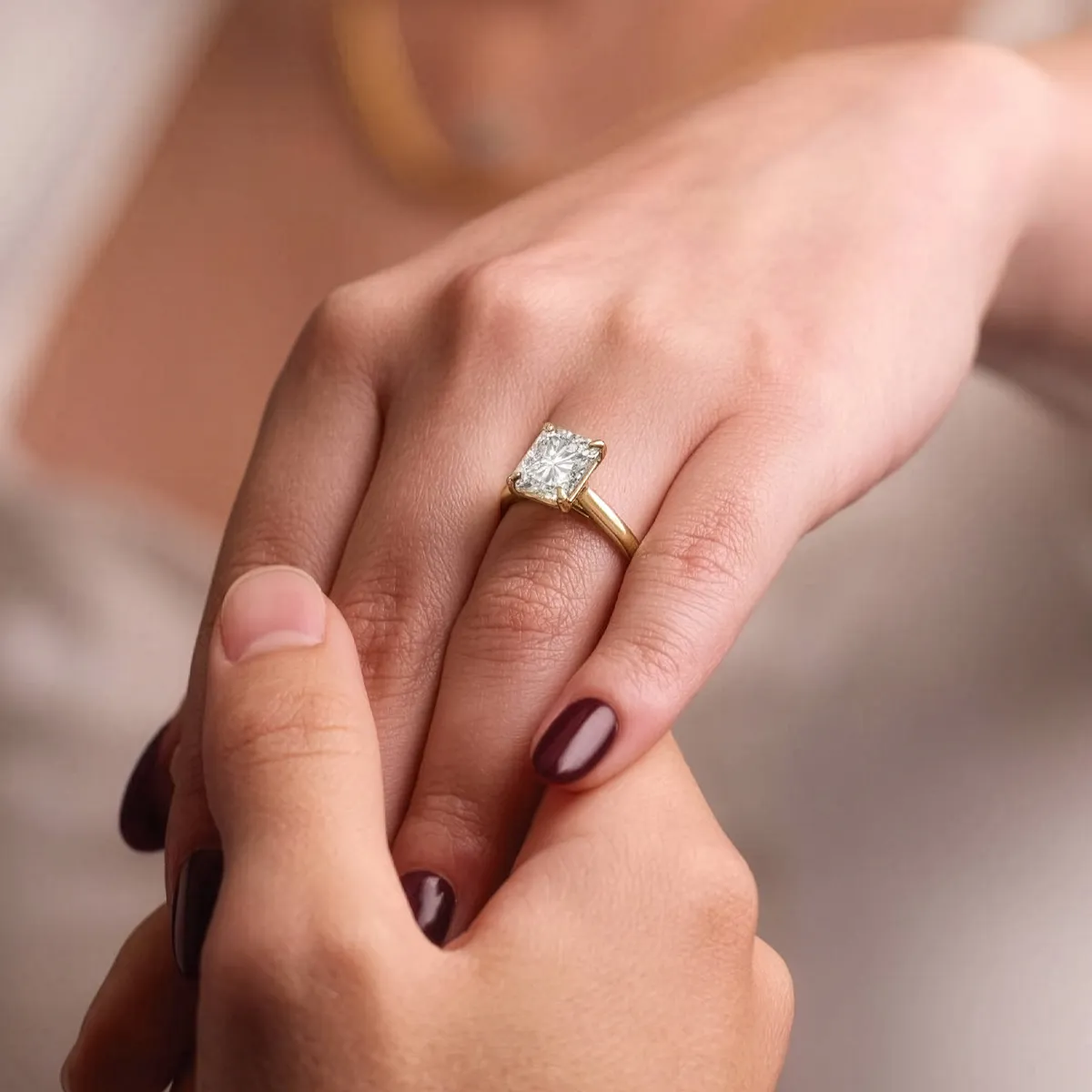 Engagement ring with a square diamond on a gold band, held by two hands. Visit Golden Gifts Jewelry in Milford.