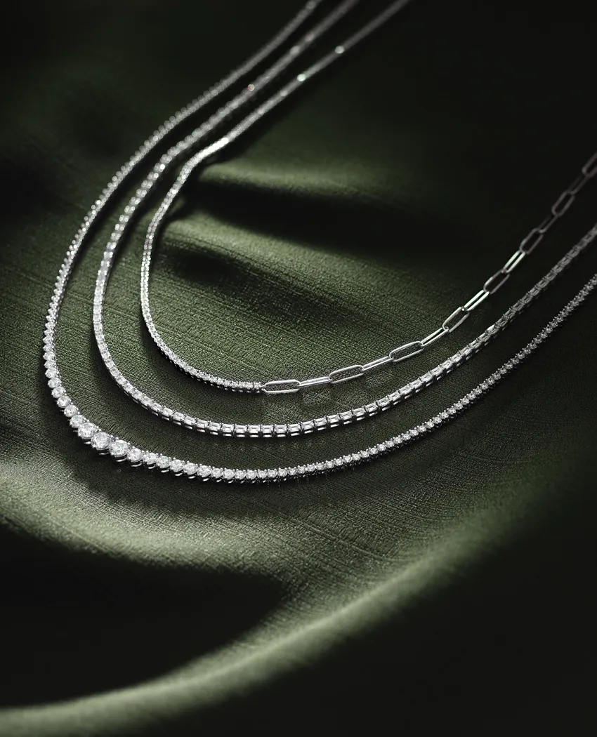 Elegant silver chains displayed on a dark green fabric background. Click to explore more chains at Golden Gifts Jewelry.