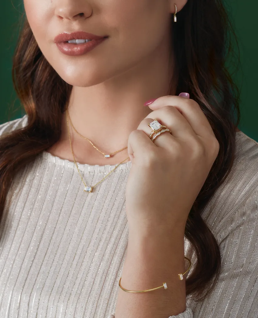 Model showcasing elegant gold jewelry including rings, necklace, and bracelet against a green background.