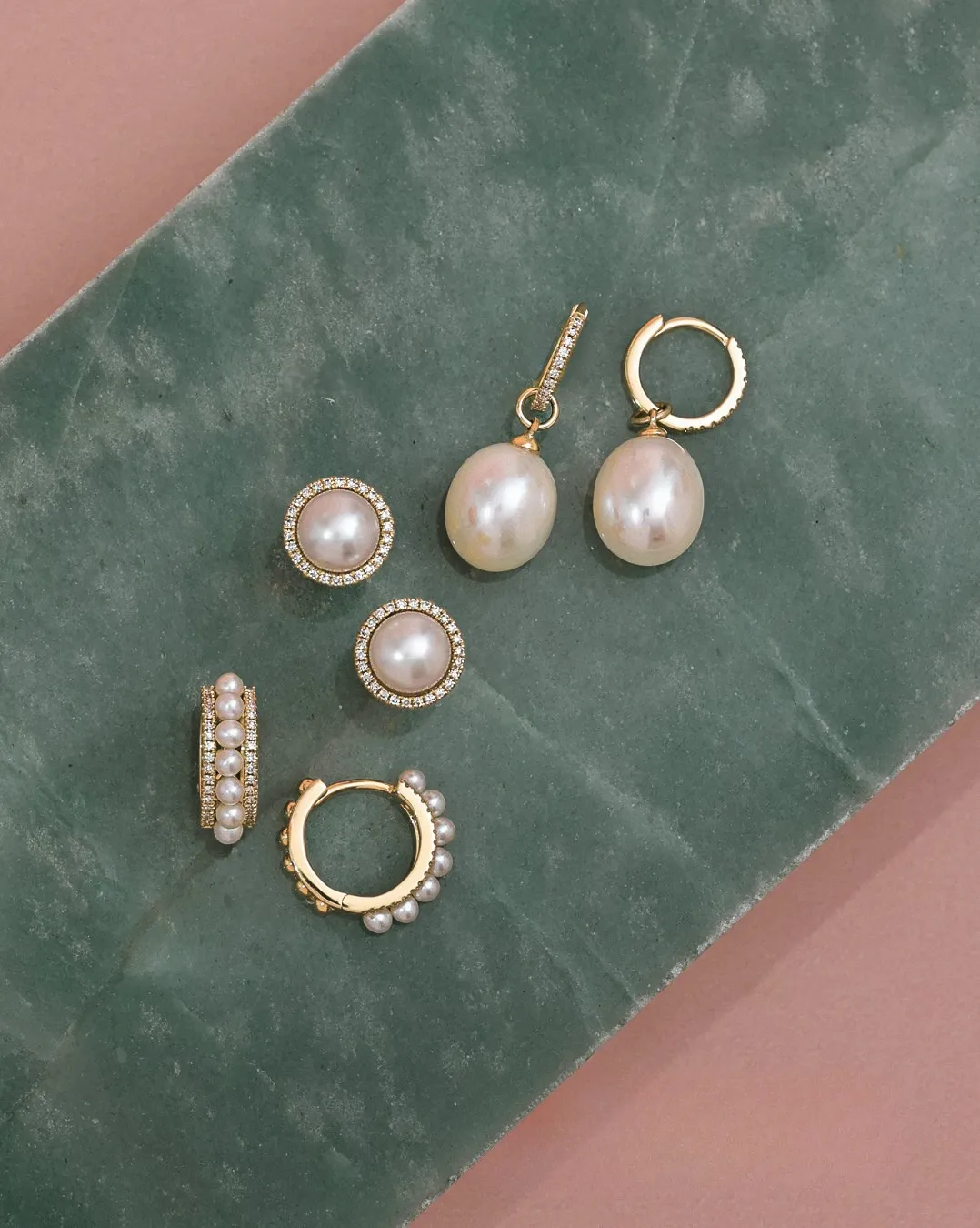 Elegant pearl earrings displayed on a green surface. Shop fine earrings at Gray's Jewelers Bespoke.