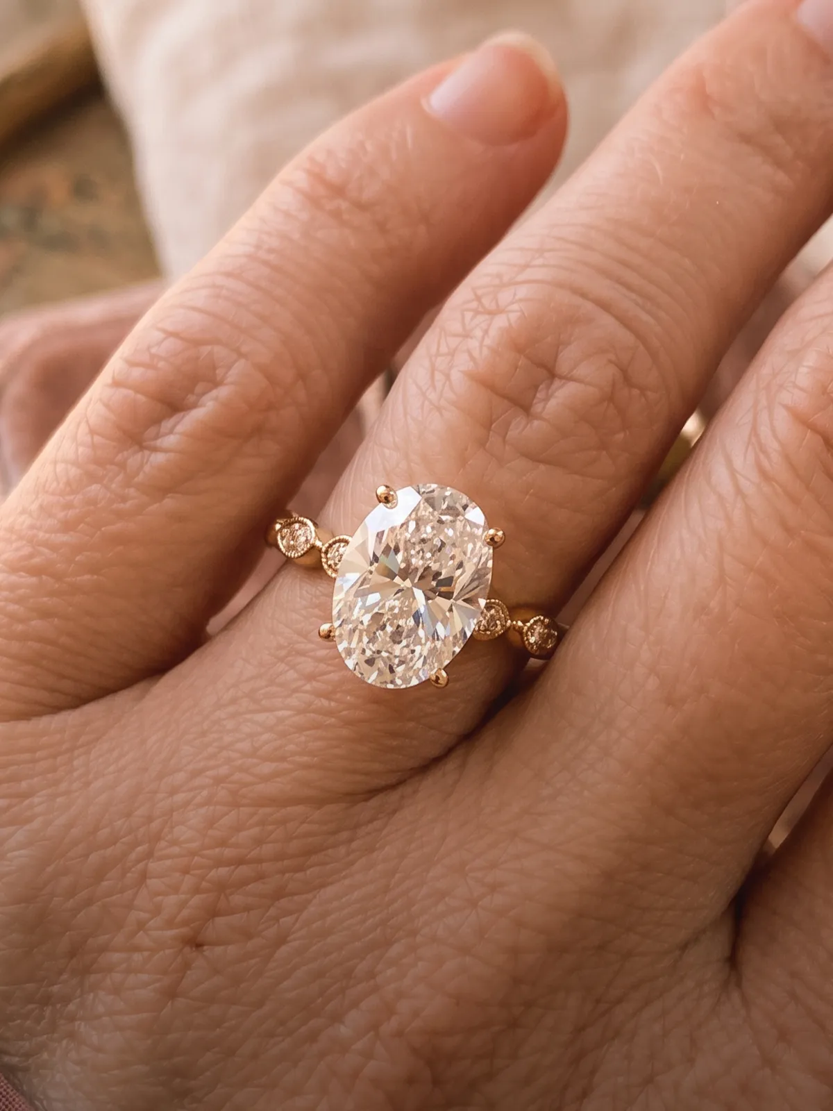 A hand wearing a gold ring with a large oval diamond and smaller side stones.