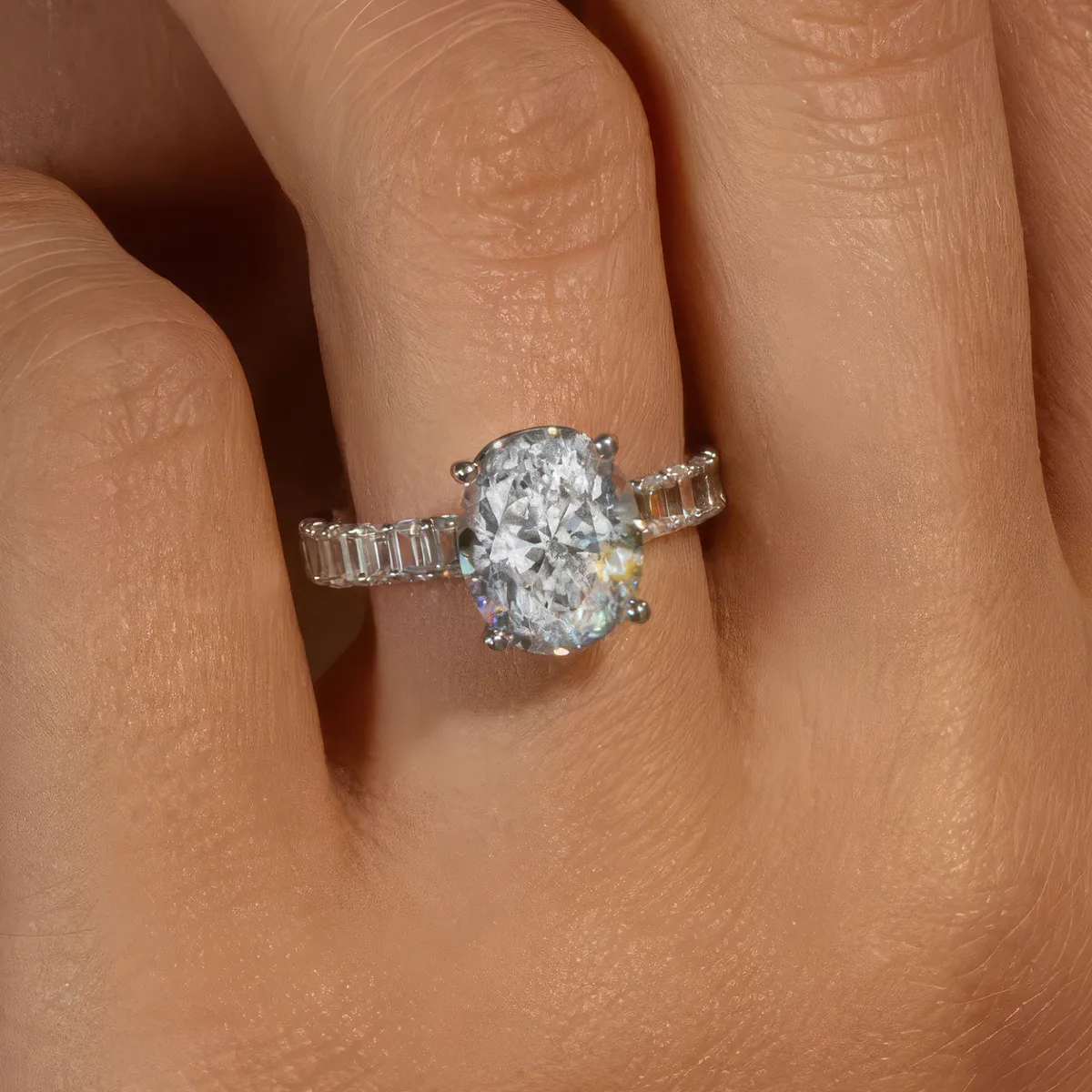 A hand wearing a diamond ring with an oval center stone and baguette side stones.