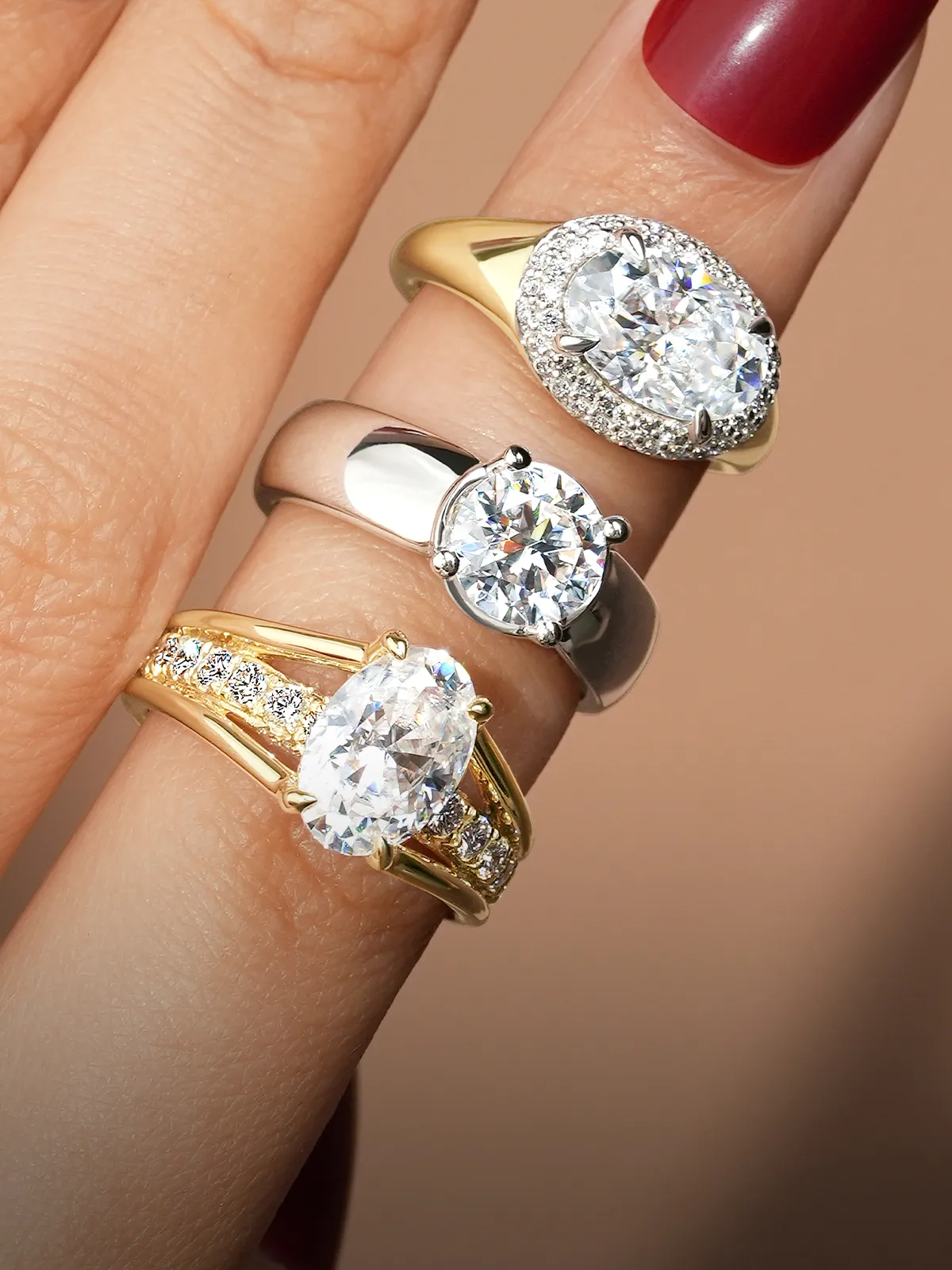 A hand displaying three diamond engagement rings with different settings.