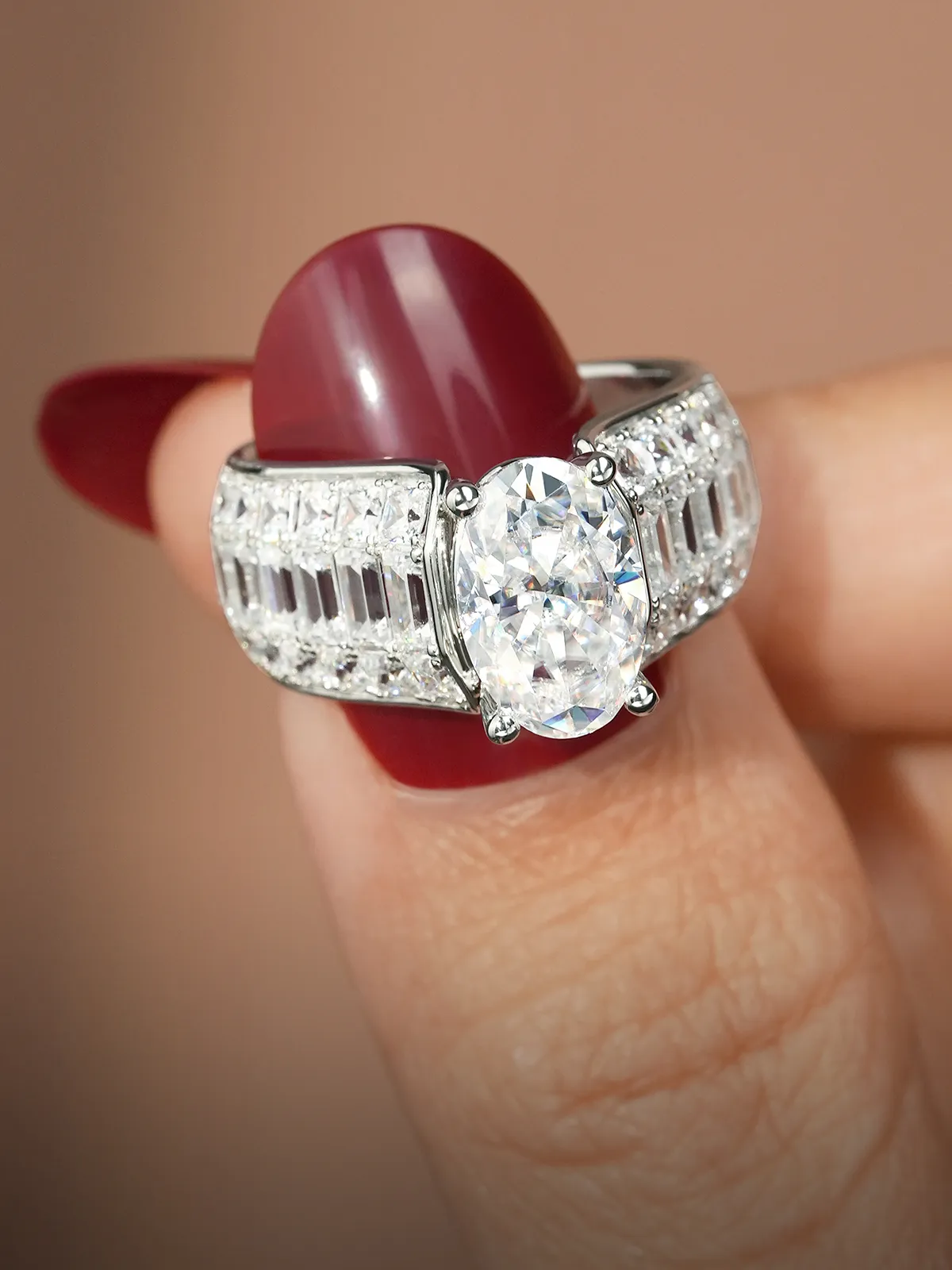 A hand holding a silver ring with a large oval diamond and detailed band.