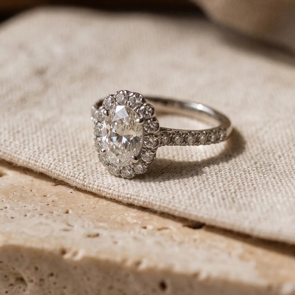 Diamond ring with halo setting on a textured fabric surface.
