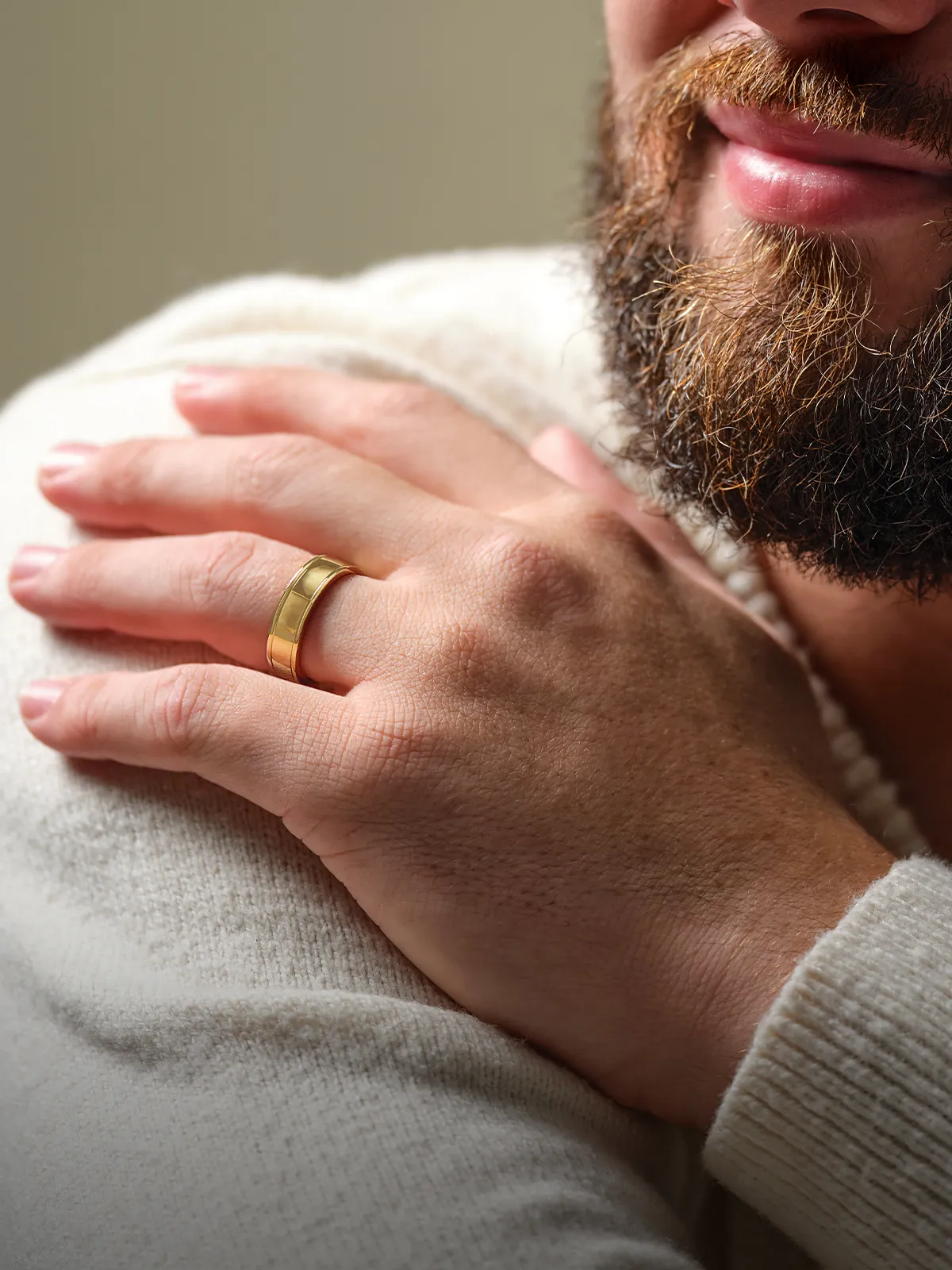 A man with a beard wearing a gold wedding band on his hand, resting on his shoulder.