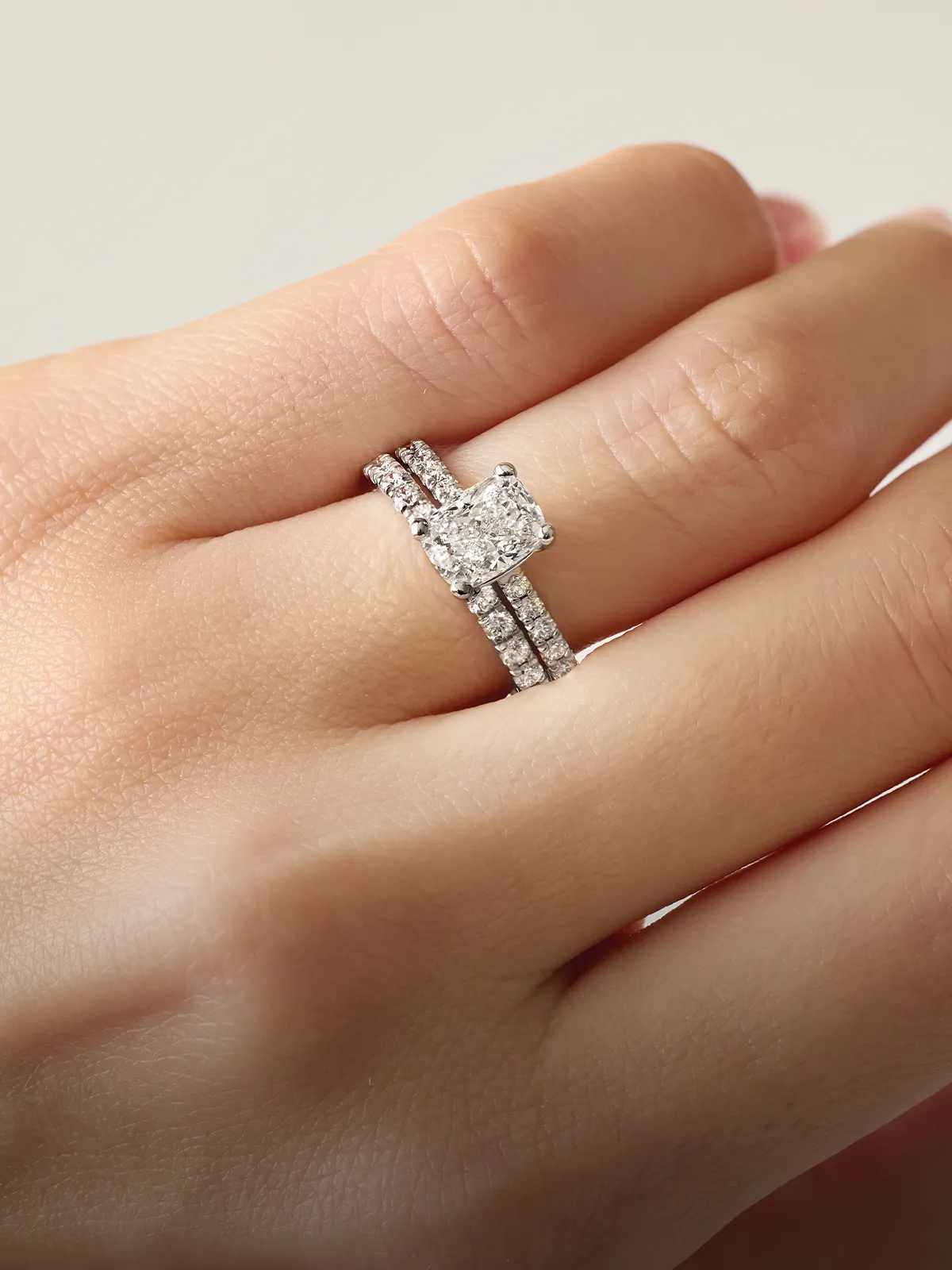 A hand wearing a diamond engagement ring and matching wedding band.