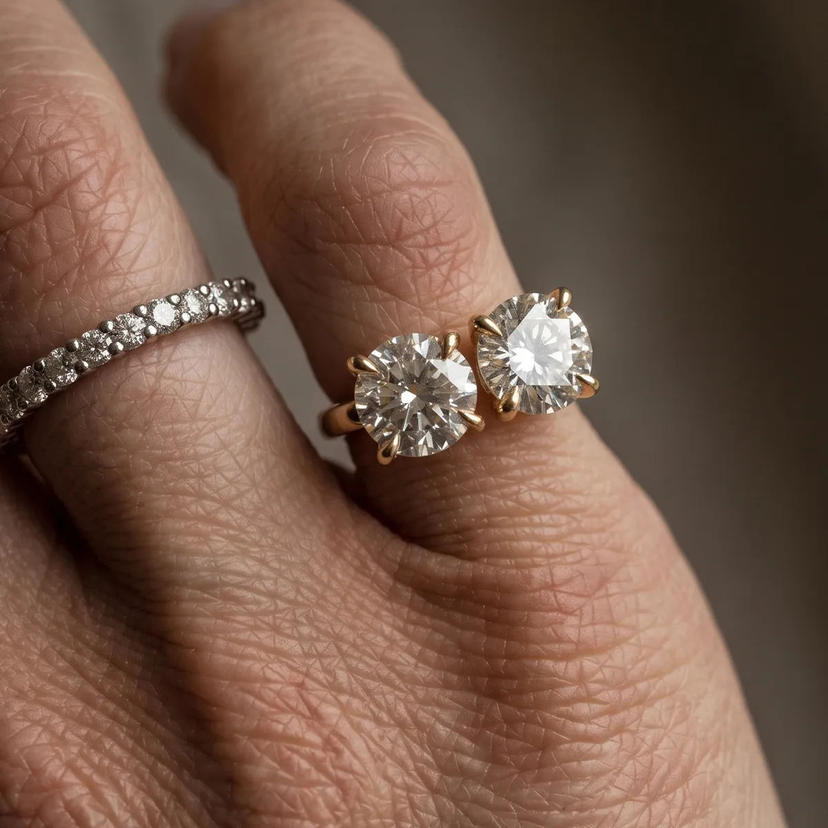 Two gold rings with large round diamonds on a finger, next to a diamond band.