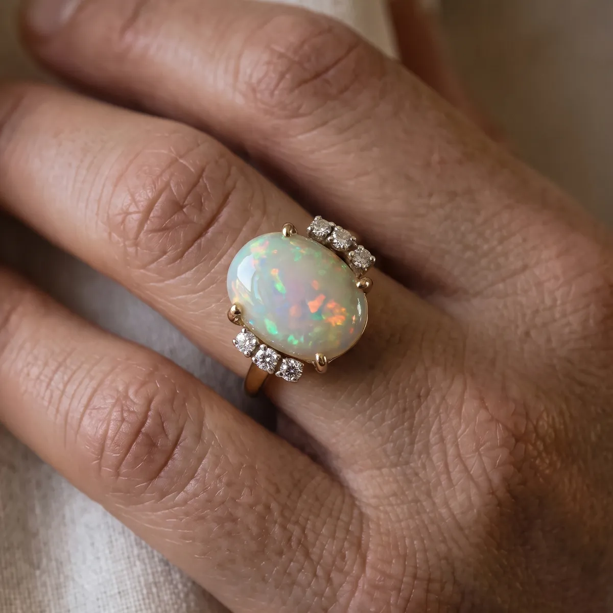 A hand wearing a gold ring with a large opal and small diamonds.