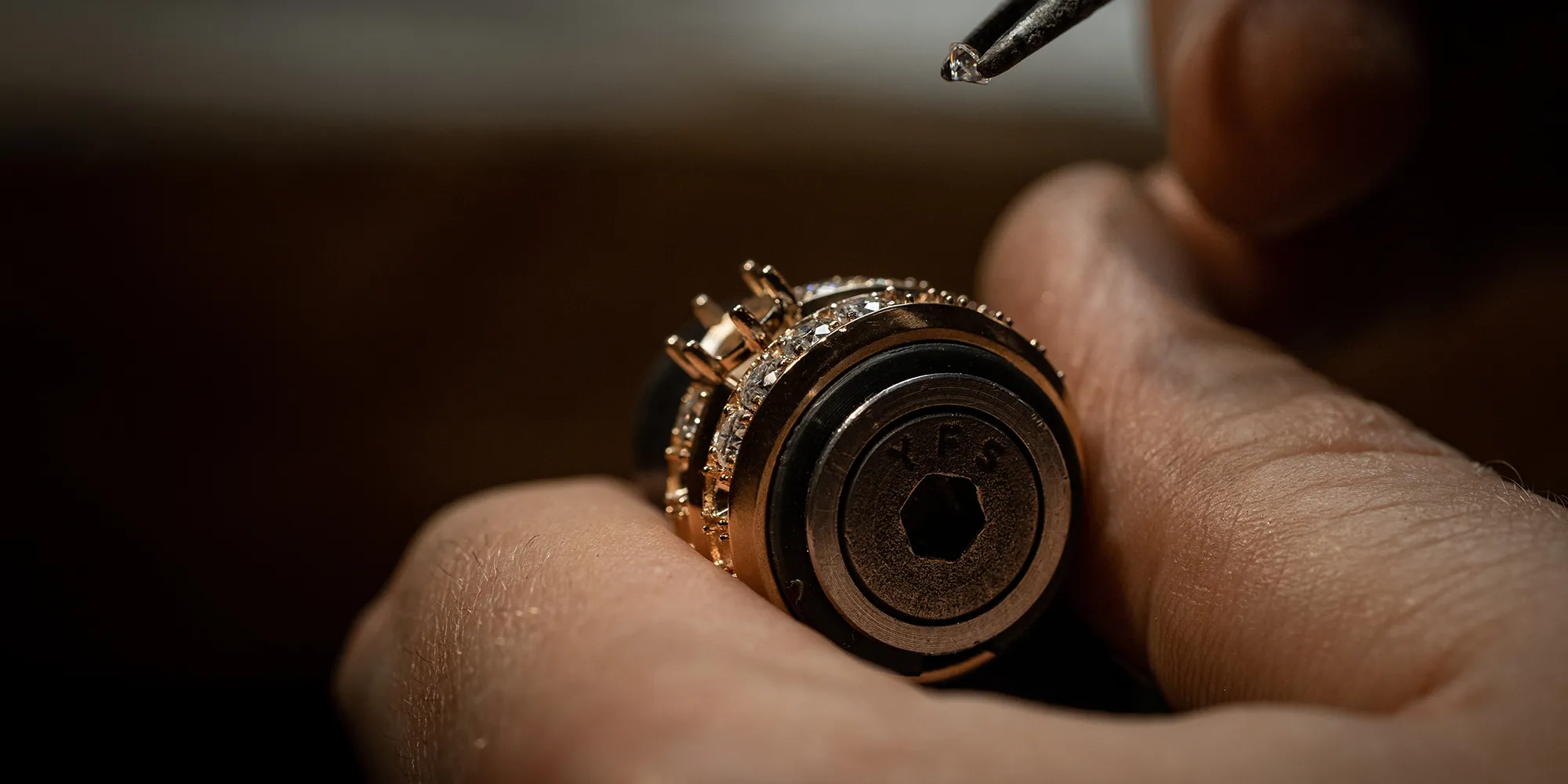 A person setting a small diamond into a gold ring using a tool.