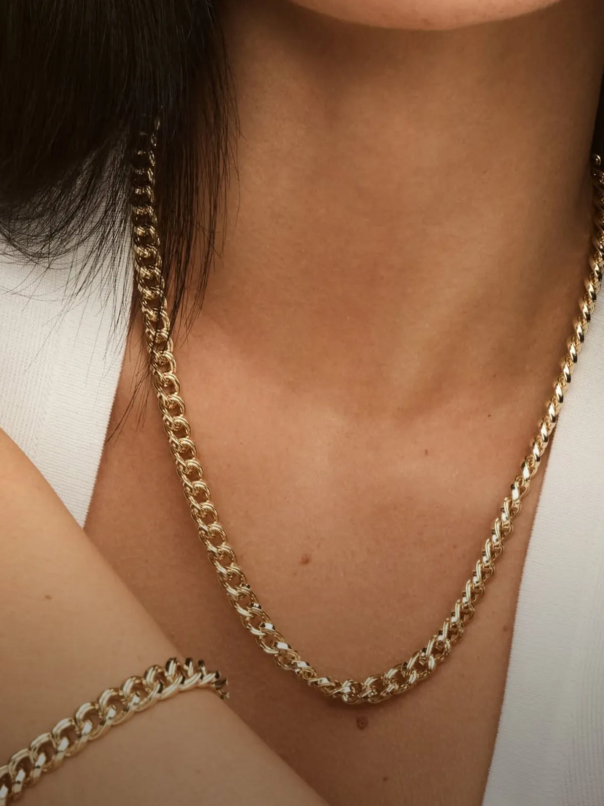 Gold chain necklace and bracelet worn on a person's neck and wrist.