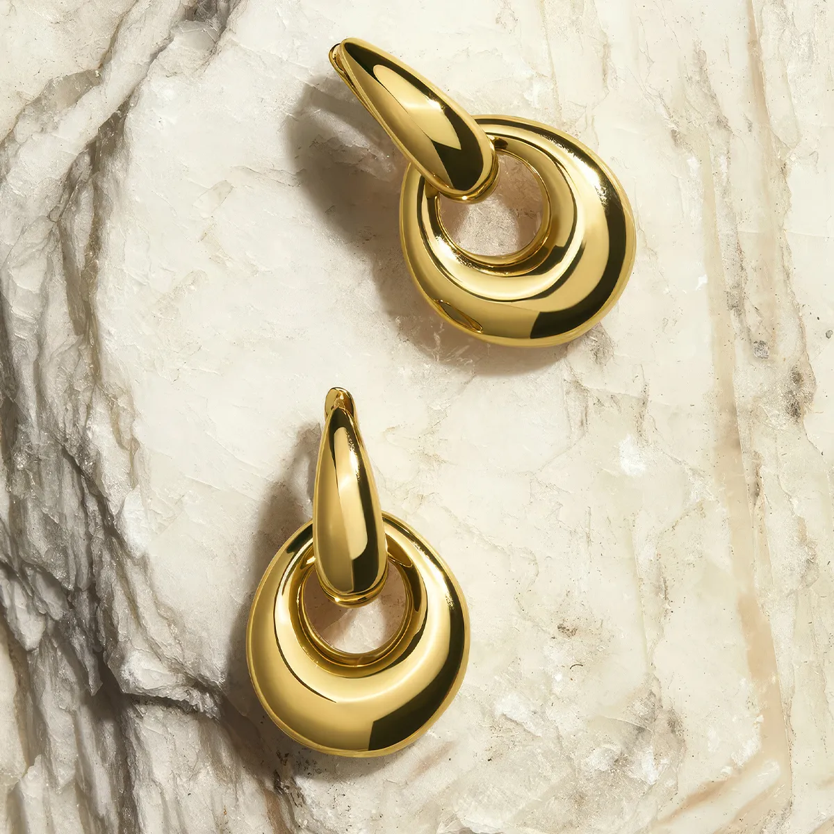 Gold hoop earrings with teardrop design on textured stone background.