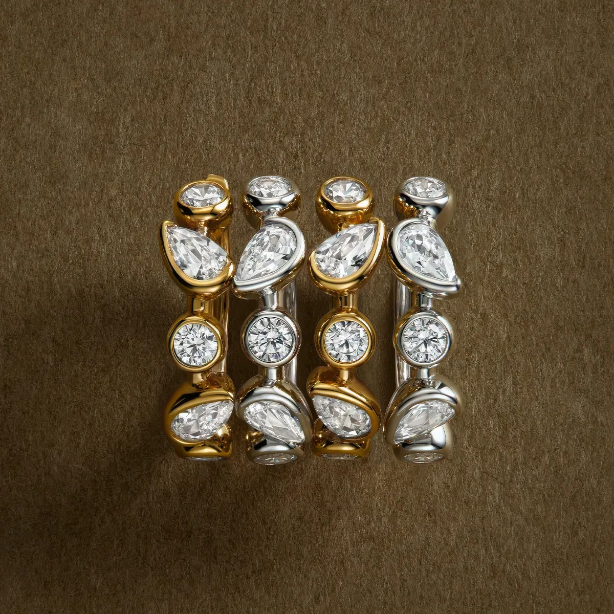 Four gold and silver rings with pear and round-cut diamonds on a brown background.