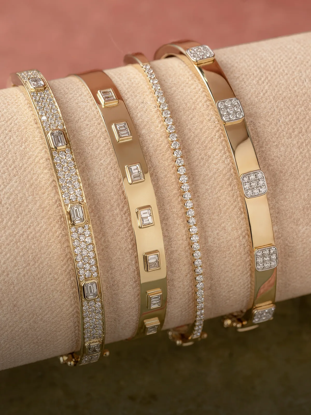 Four gold bracelets with diamond accents displayed on a beige cushion.