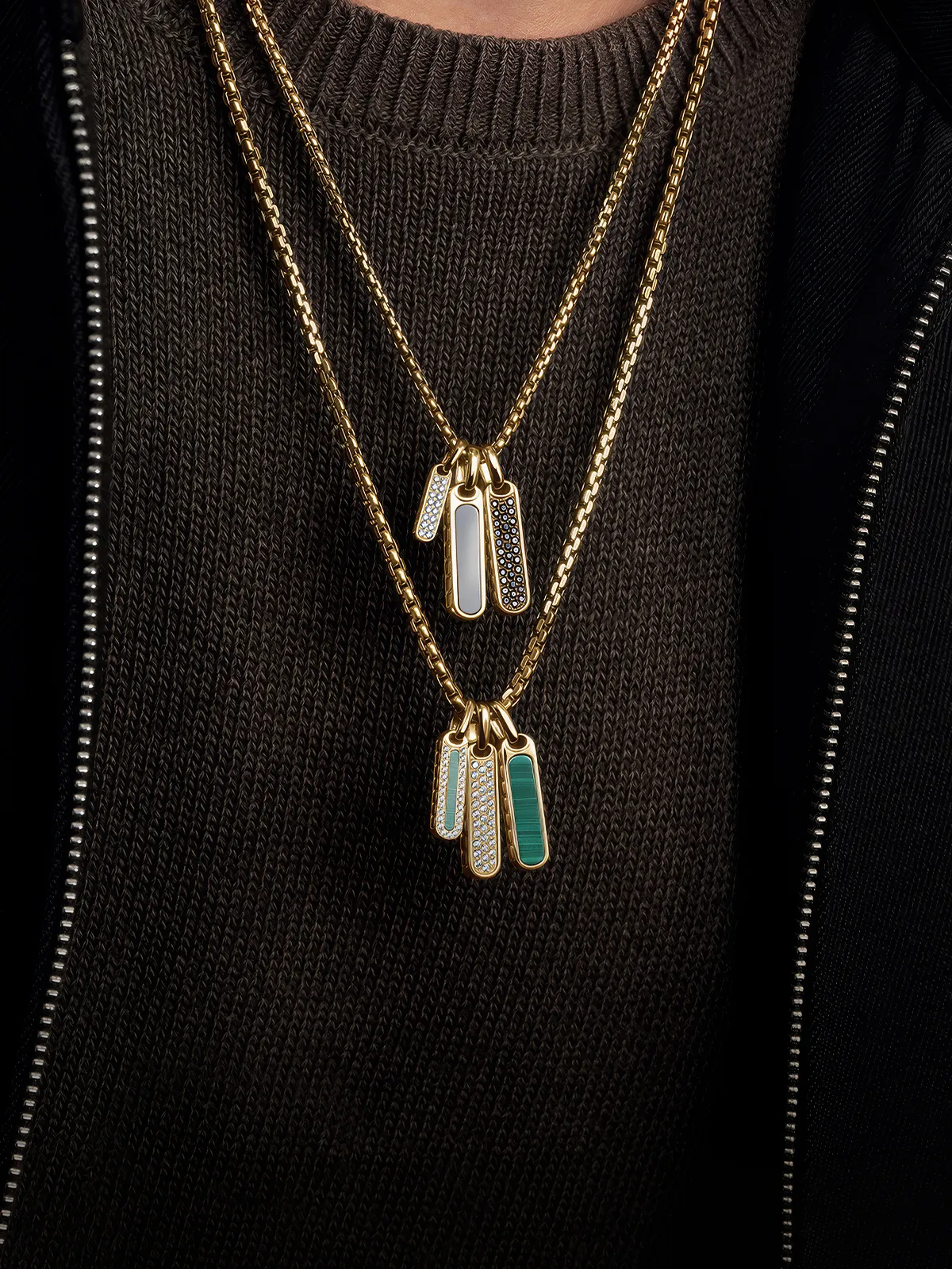 Gold necklaces with rectangular pendants inlaid with stones, worn over a dark sweater.