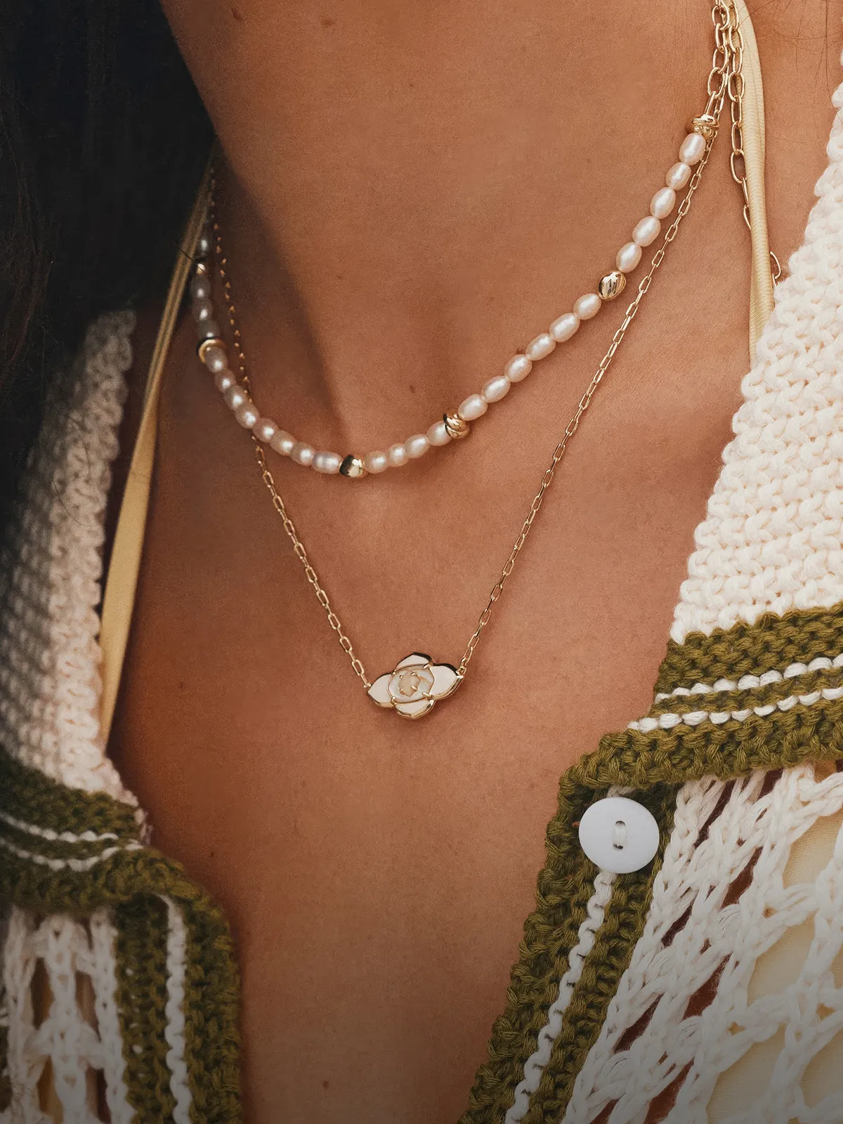Layered gold and pearl necklaces on a woman's neck, wearing a crochet top.