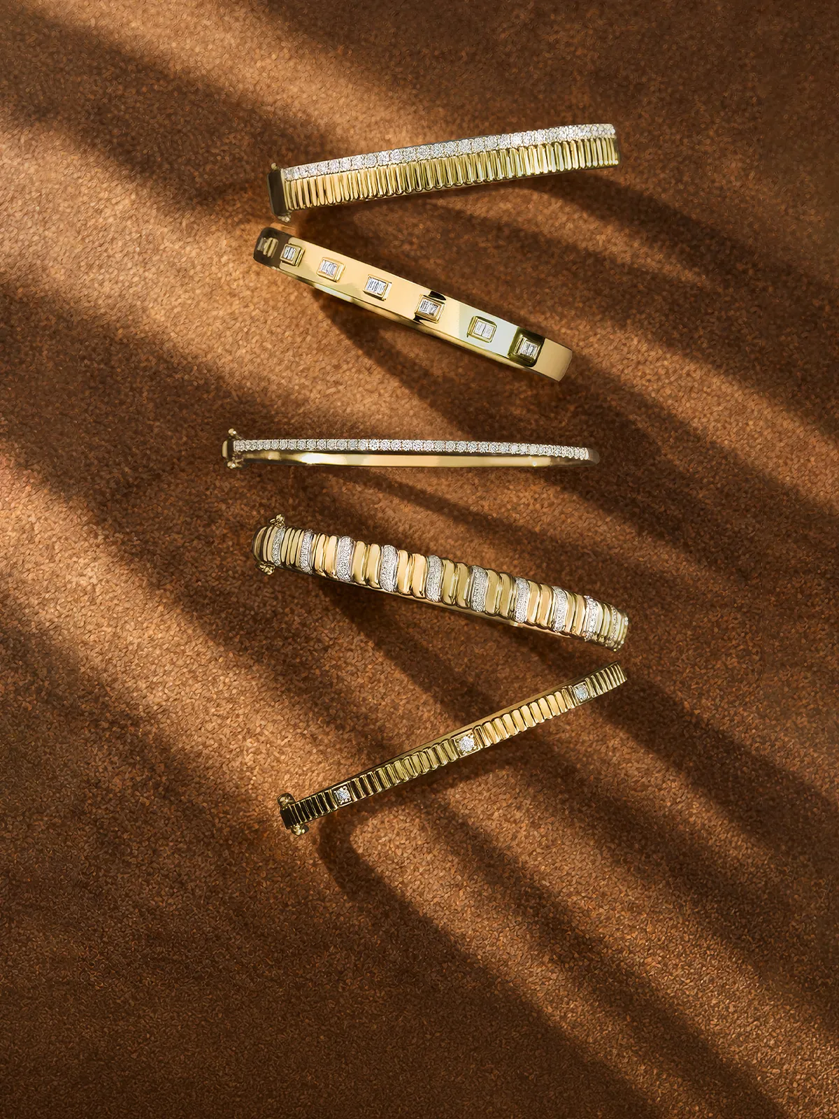 A wrist adorned with multiple gold and silver bracelets featuring diamond accents.