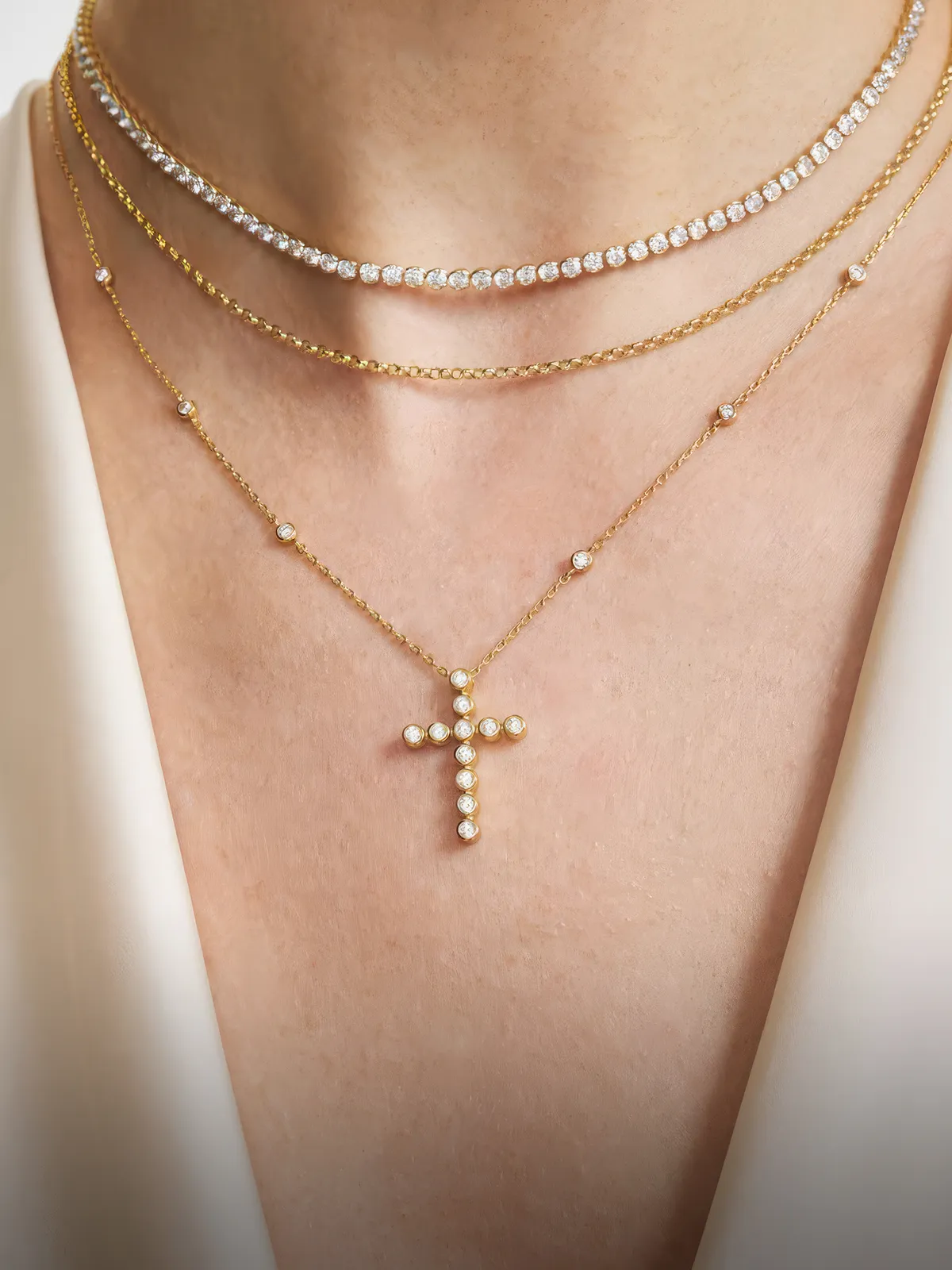Layered gold and diamond necklaces with a cross pendant on a woman's neck.