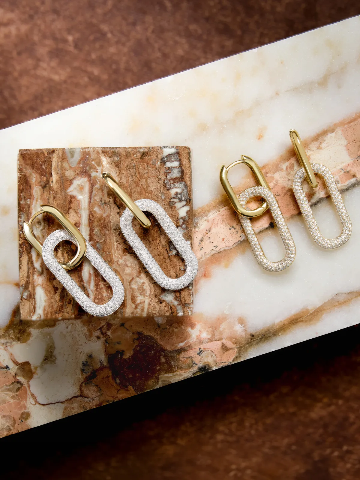 Gold and diamond link earrings on a marble surface.