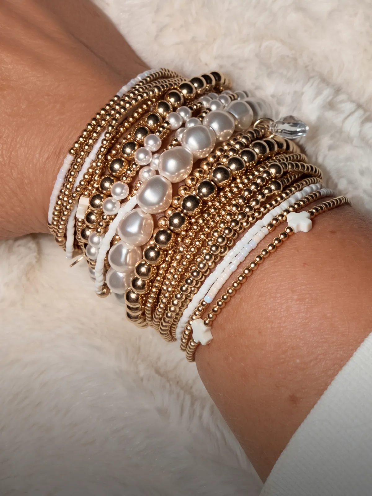 A wrist adorned with multiple gold and pearl bracelets on a light background.