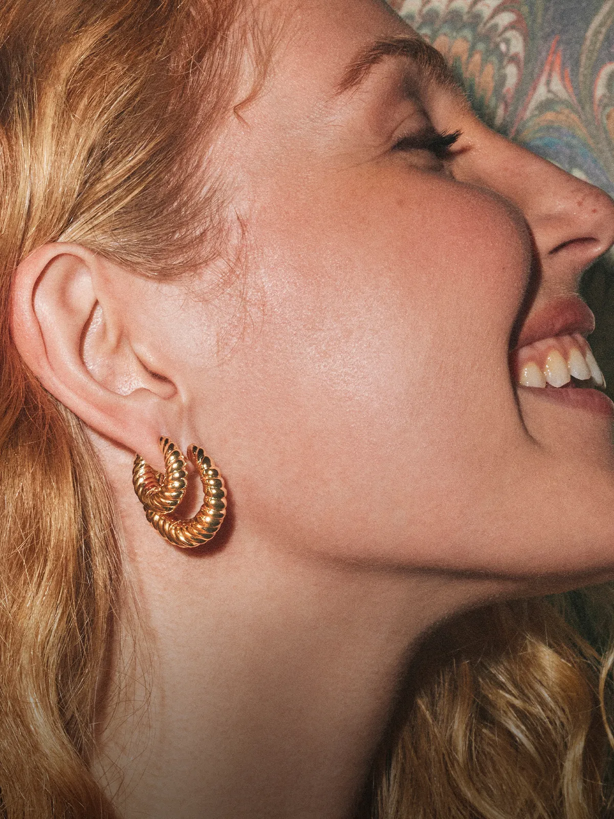 A woman with gold hoop earrings smiles, showing her profile.