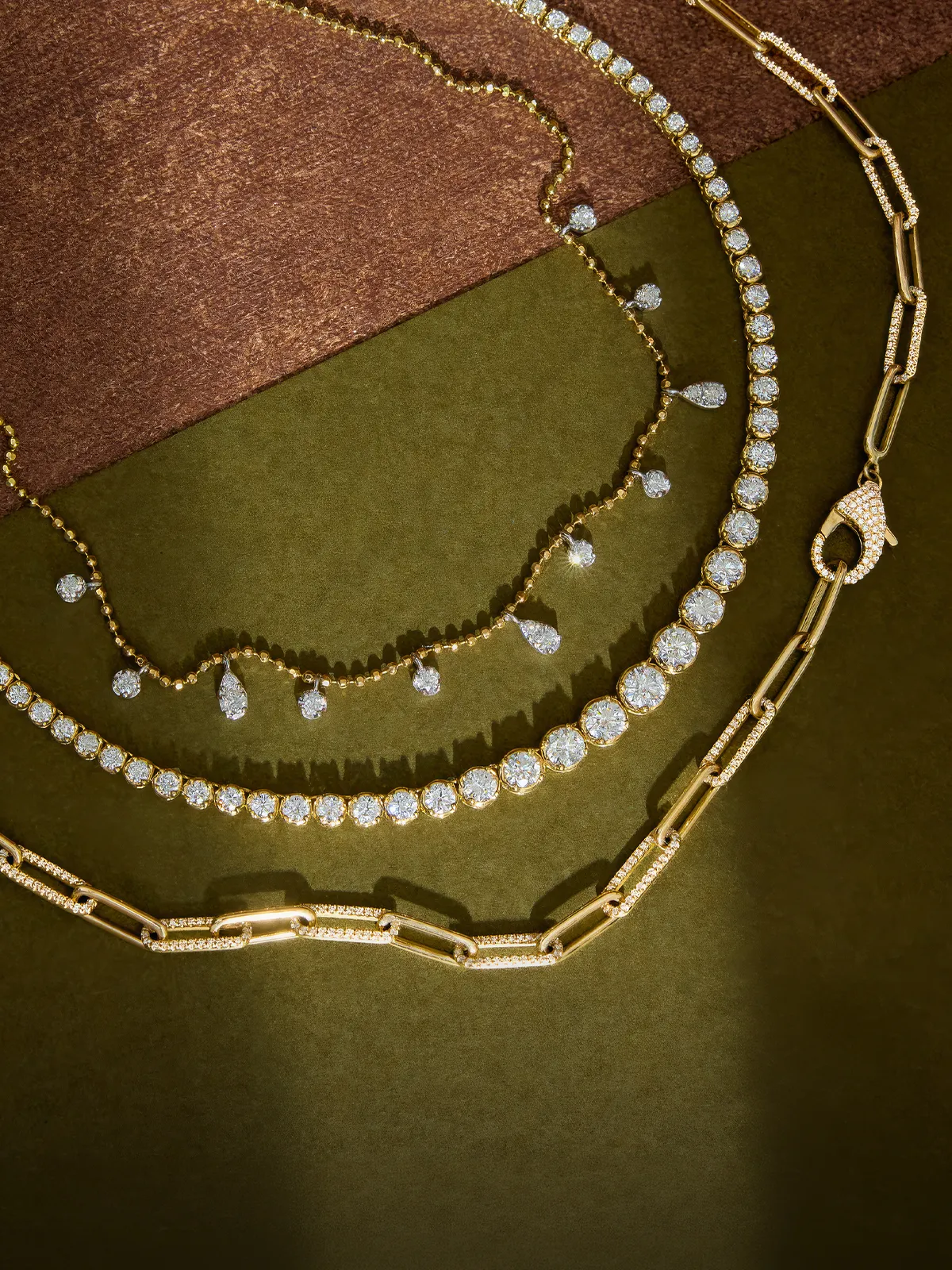 Three gold necklaces with diamonds on a textured brown and green background.