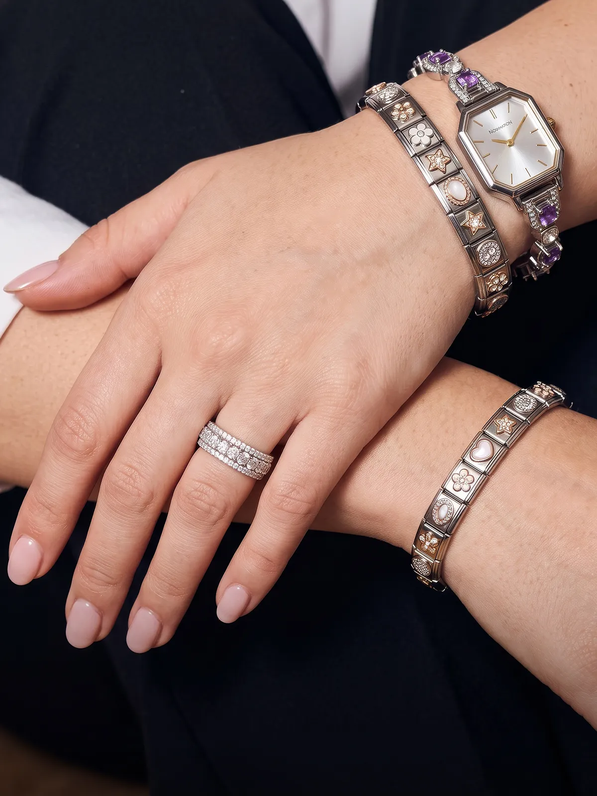 A person wearing layered silver necklaces and multiple bracelets with charms on their wrist.