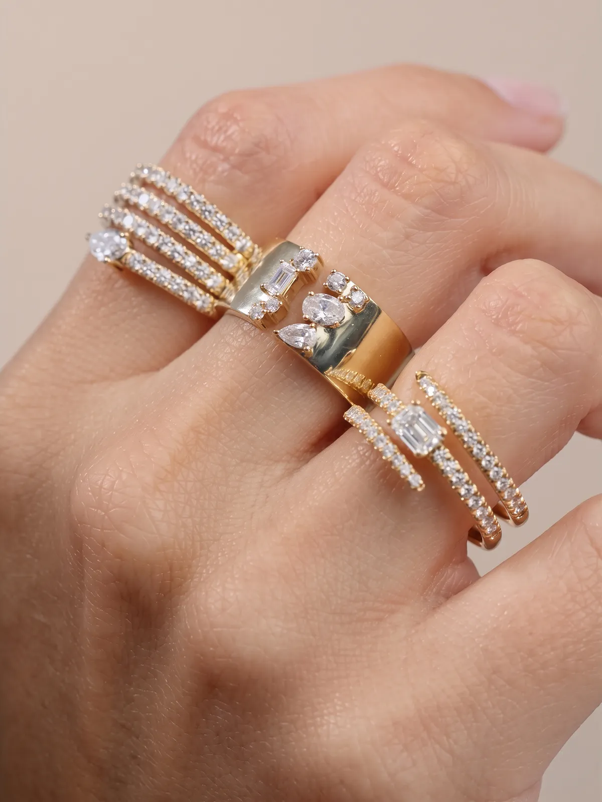 A hand wearing multiple gold rings with diamonds on different fingers.