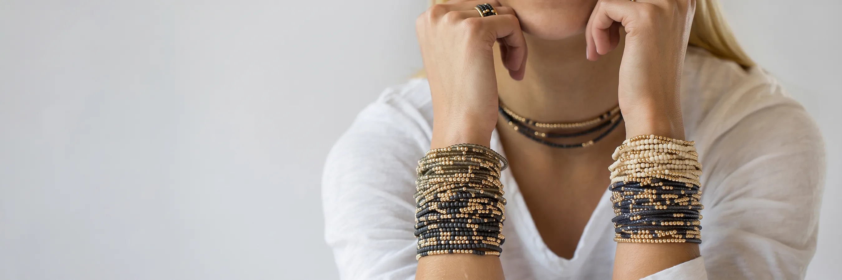 A person wearing multiple beaded bracelets and a necklace, resting their chin on their hands.