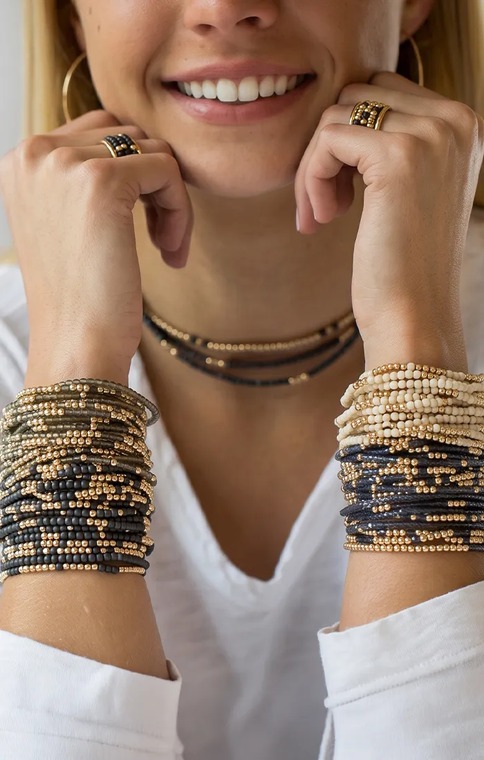 A person wearing multiple beaded bracelets and a necklace, resting their chin on their hands.