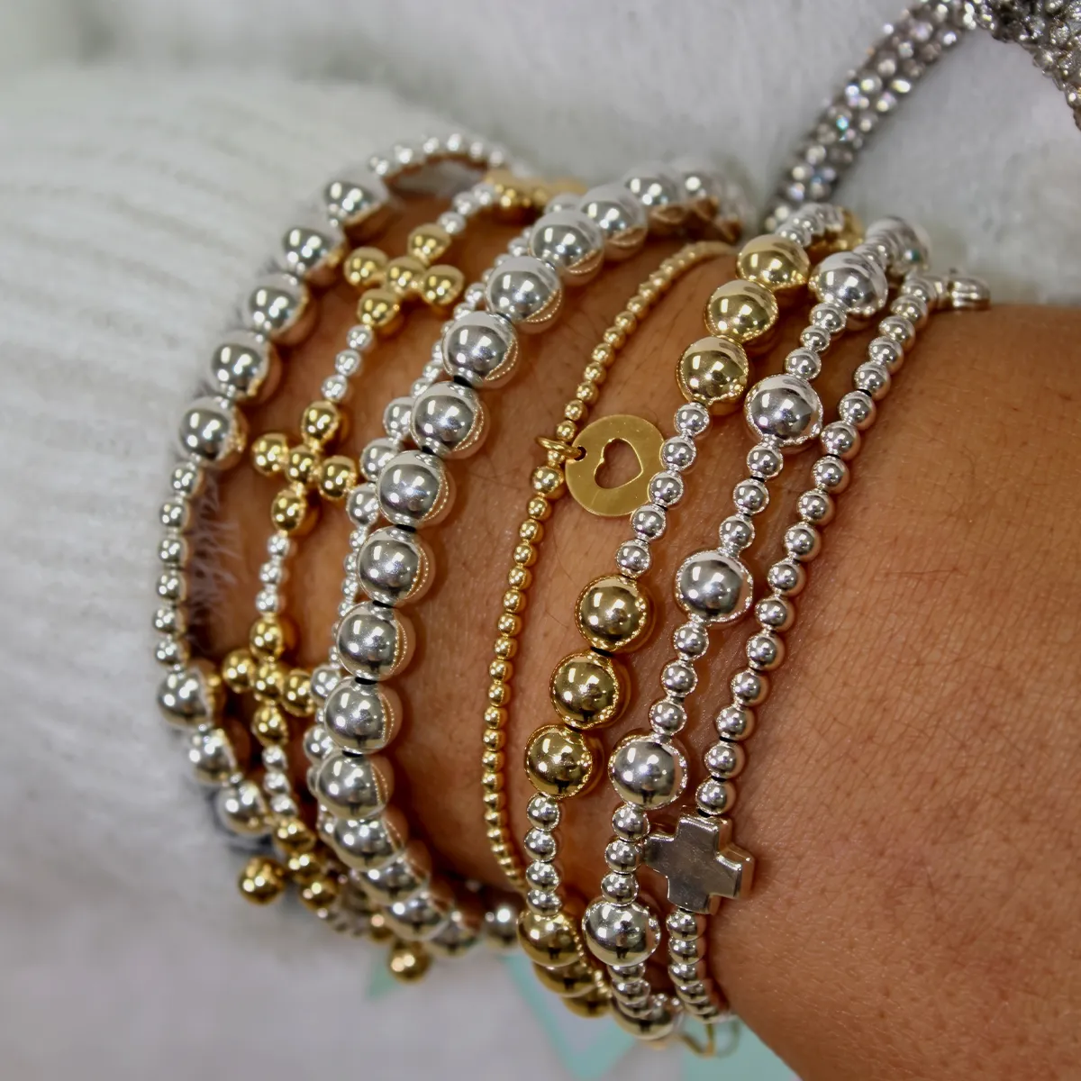 A wrist adorned with multiple gold and silver beaded bracelets.