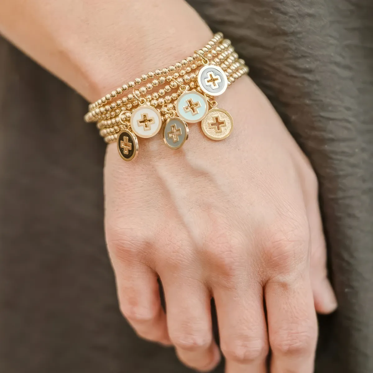 A hand wearing multiple gold beaded bracelets with cross charms.