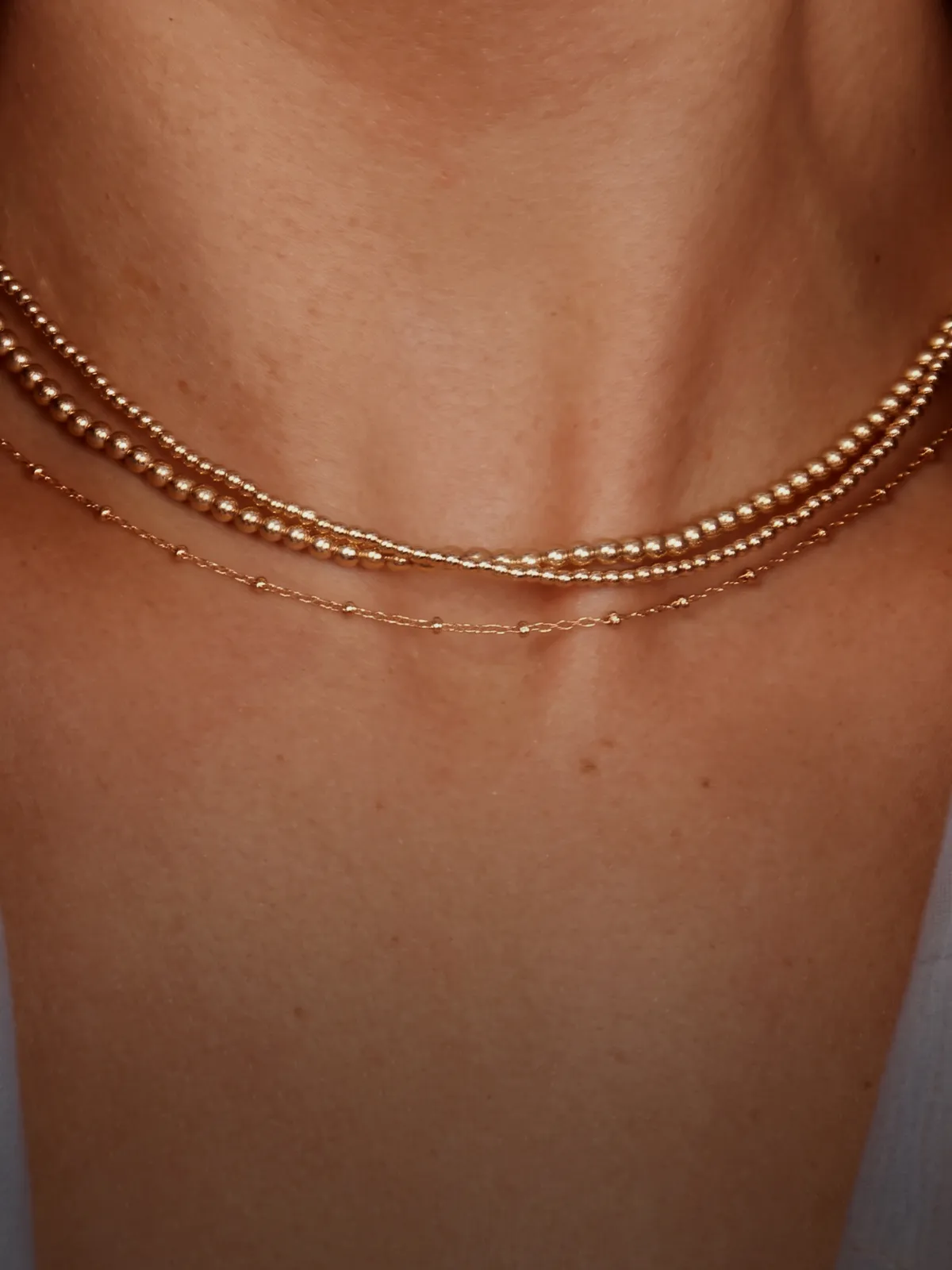Two delicate gold necklaces layered on a person's neck.