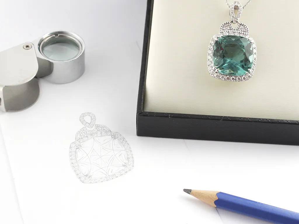 Sketch on paper of blue cushion cut gemstone pendant and finished custom jewellery piece sitting in presentation box
