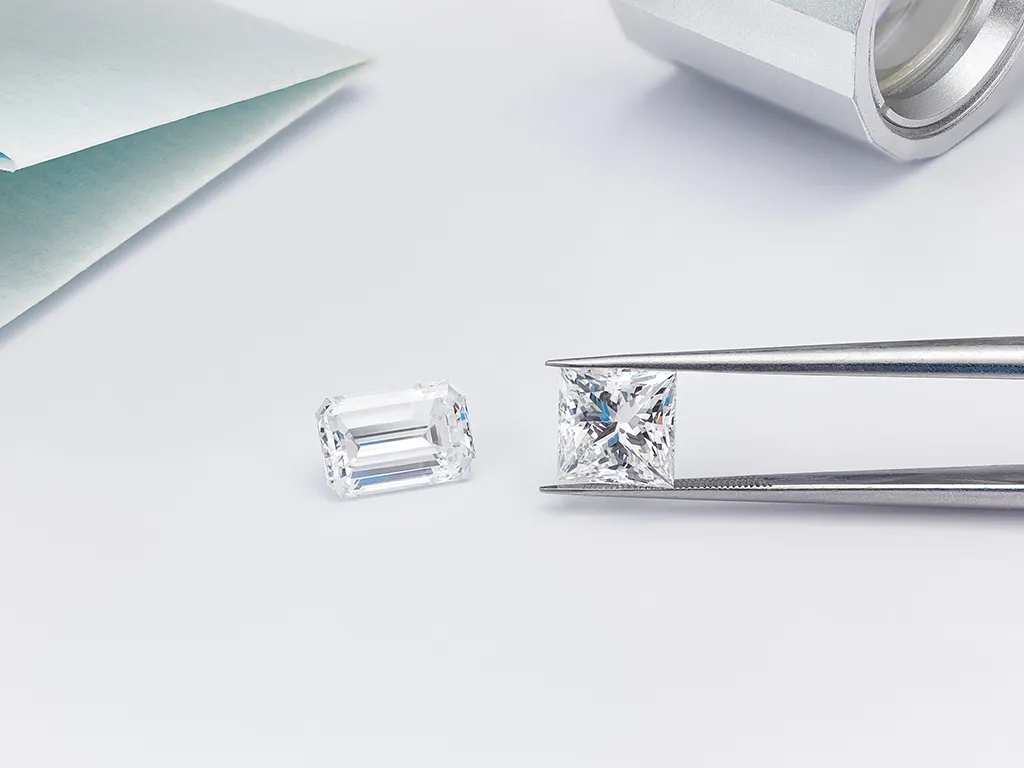 Emerald cut and princess cut diamond being held by jewellers tweezers
