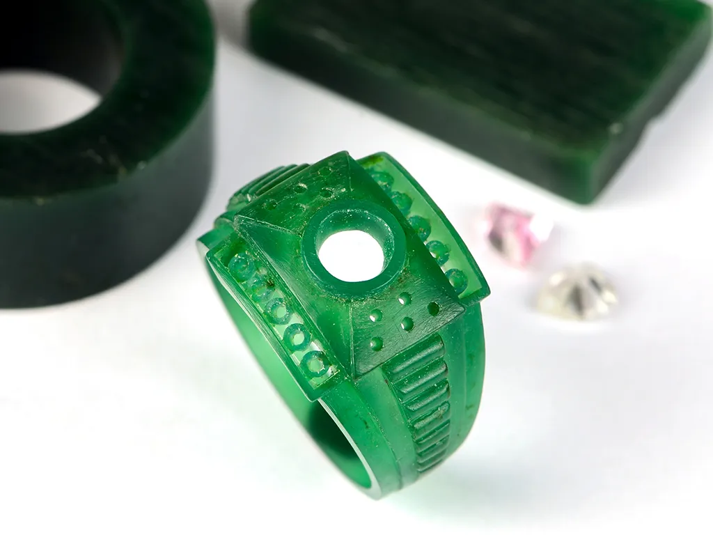 Wax mold of a fancy ring sitting on a table with loose gemstones