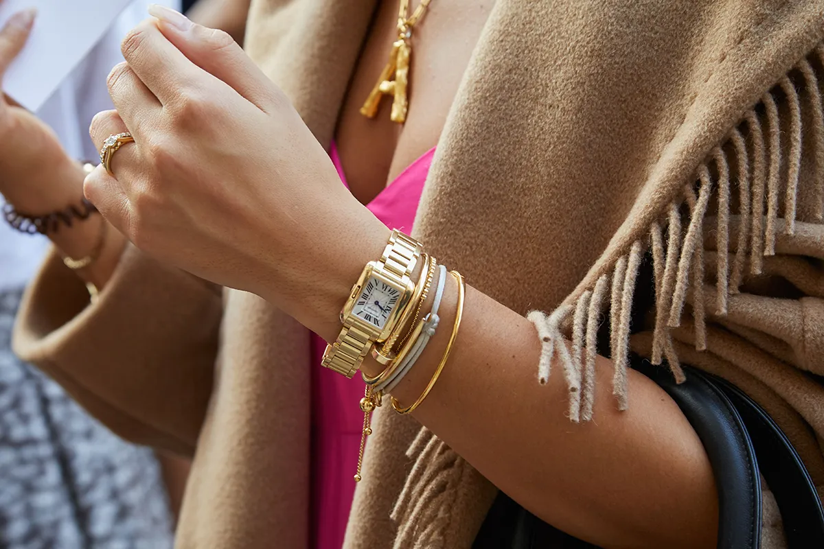 Woman wearing a brown fringe poncho and yellow gold Cartier Santos with white dial 