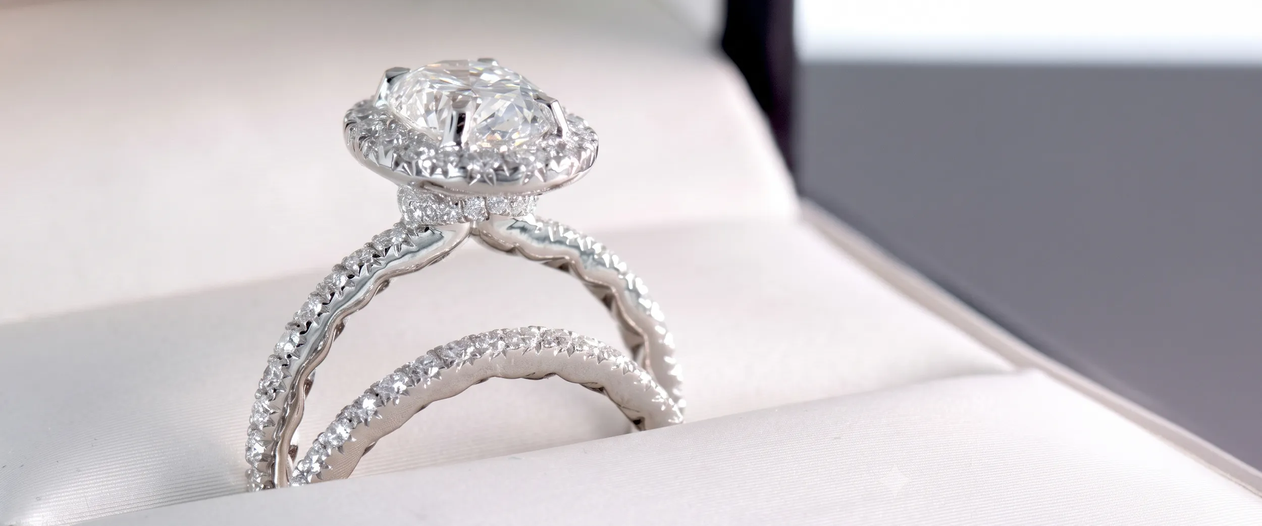 A close-up of a diamond engagement ring with a matching diamond band on a white surface.