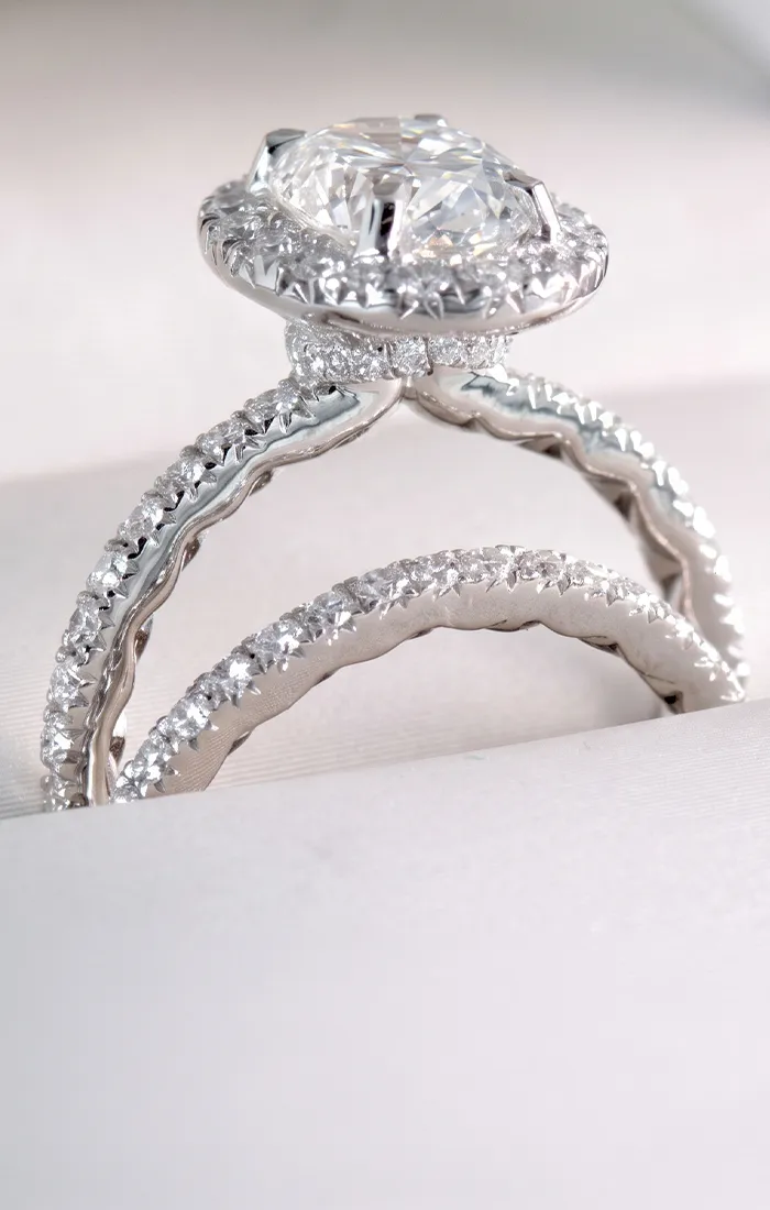 A close-up of a diamond engagement ring with a matching diamond band on a white surface.