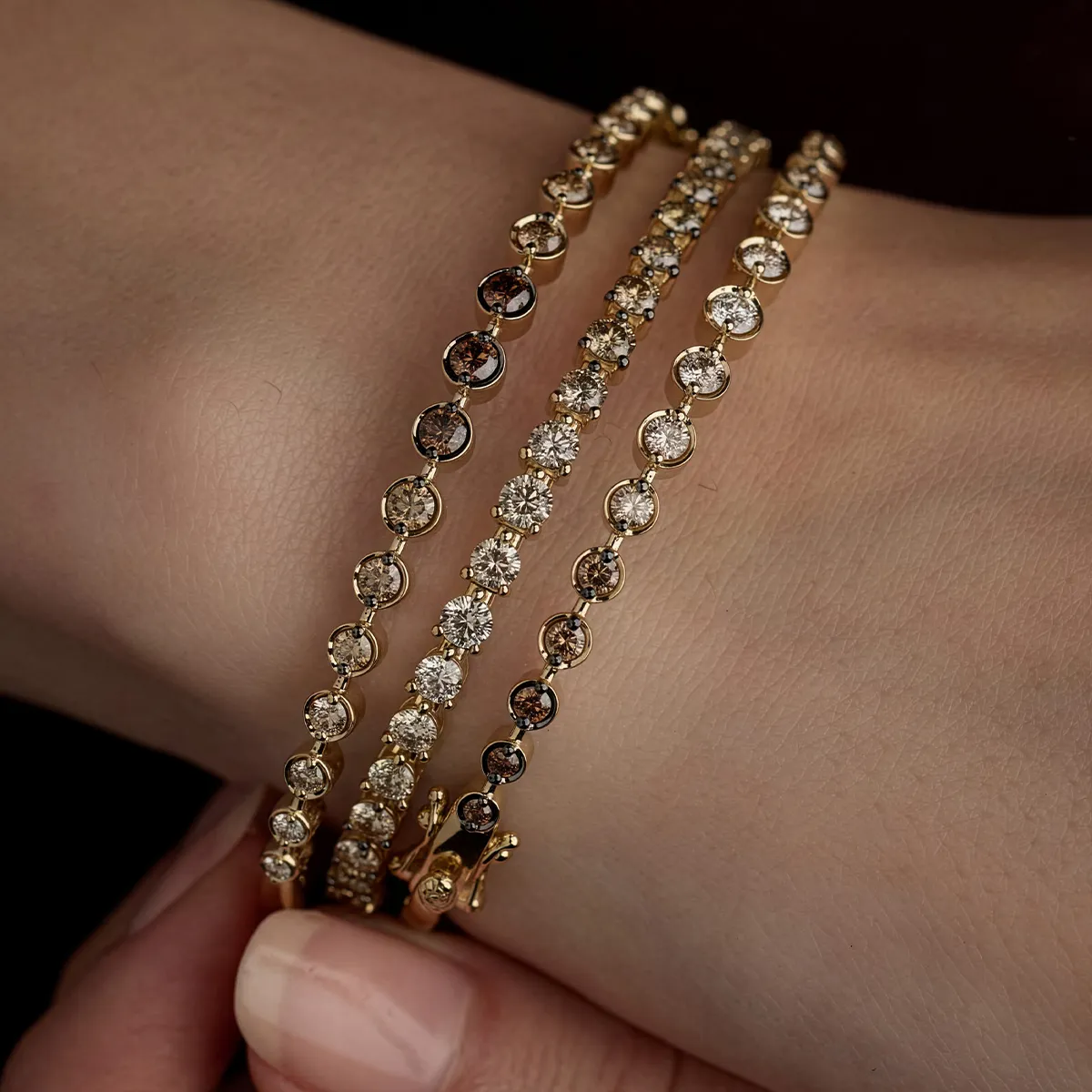 Three gold bracelets with round diamonds on a wrist, showcasing elegant jewelry design.