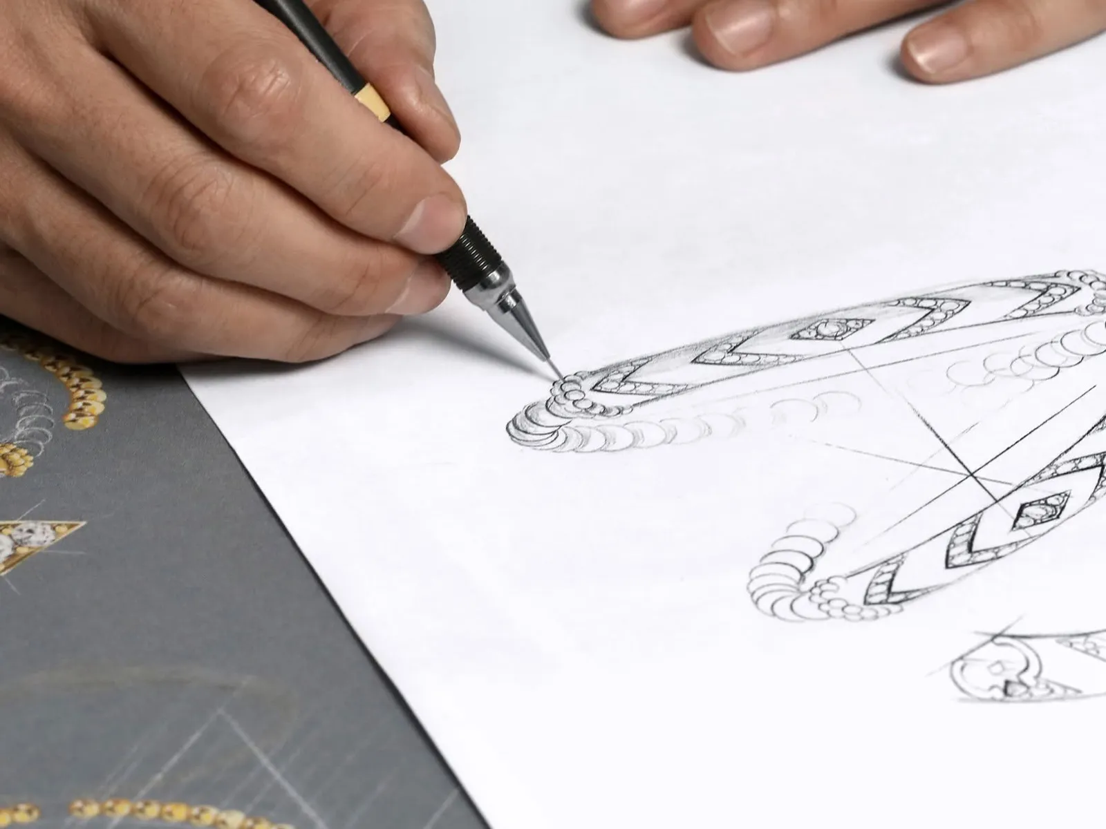Hand drawing intricate jewelry design with a pencil on paper.