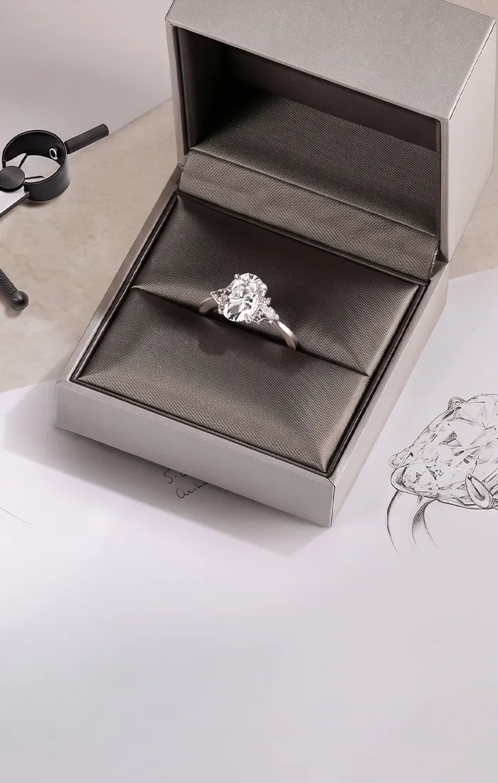 A diamond ring in a box with design sketches and a drafting compass nearby.