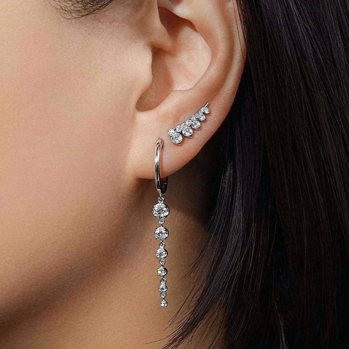 A close-up of an ear wearing a diamond ear climber and a dangling diamond earring.