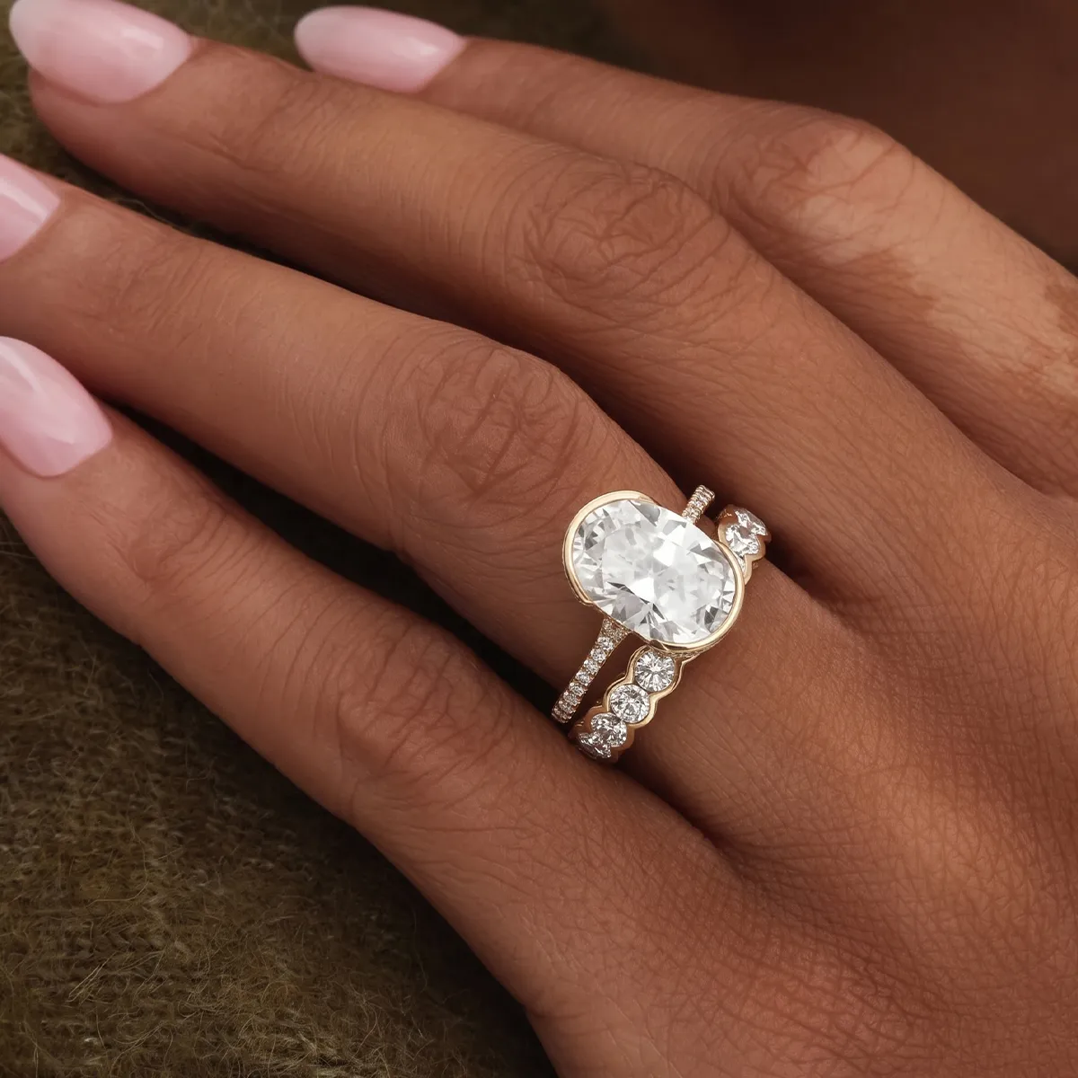 A hand with manicured nails wearing a gold ring with a large oval diamond and smaller diamonds.
