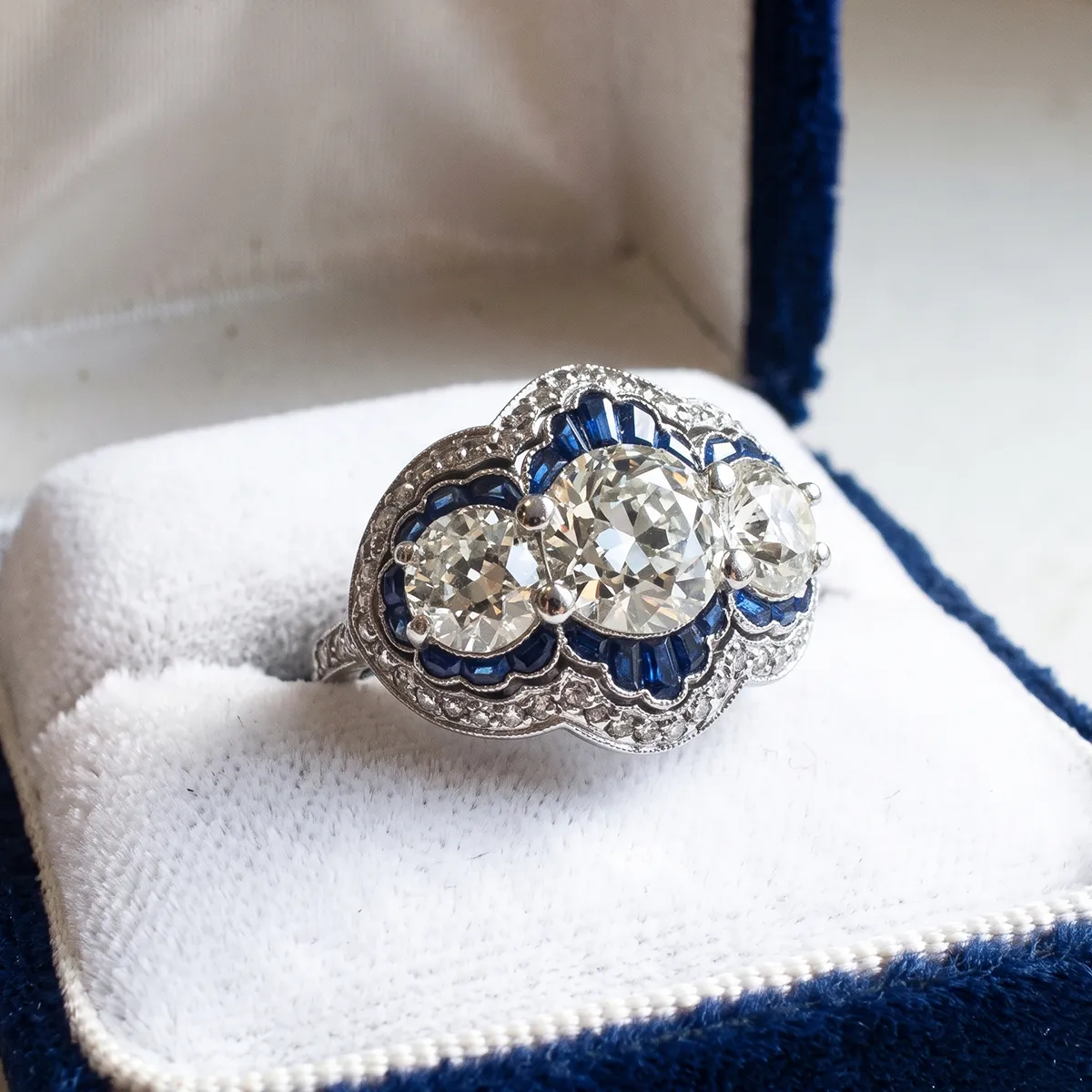An ornate diamond and sapphire ring in a blue velvet box.