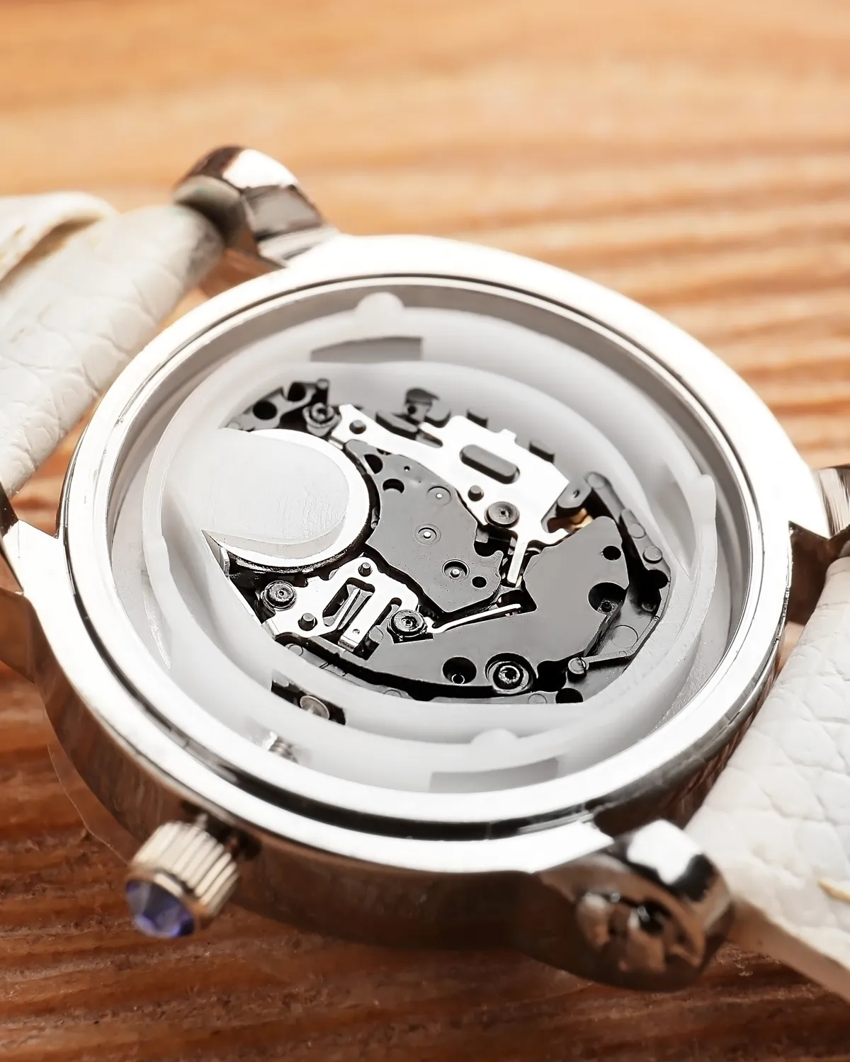 Close-up of a watch's internal mechanism with a white strap on a wooden surface.