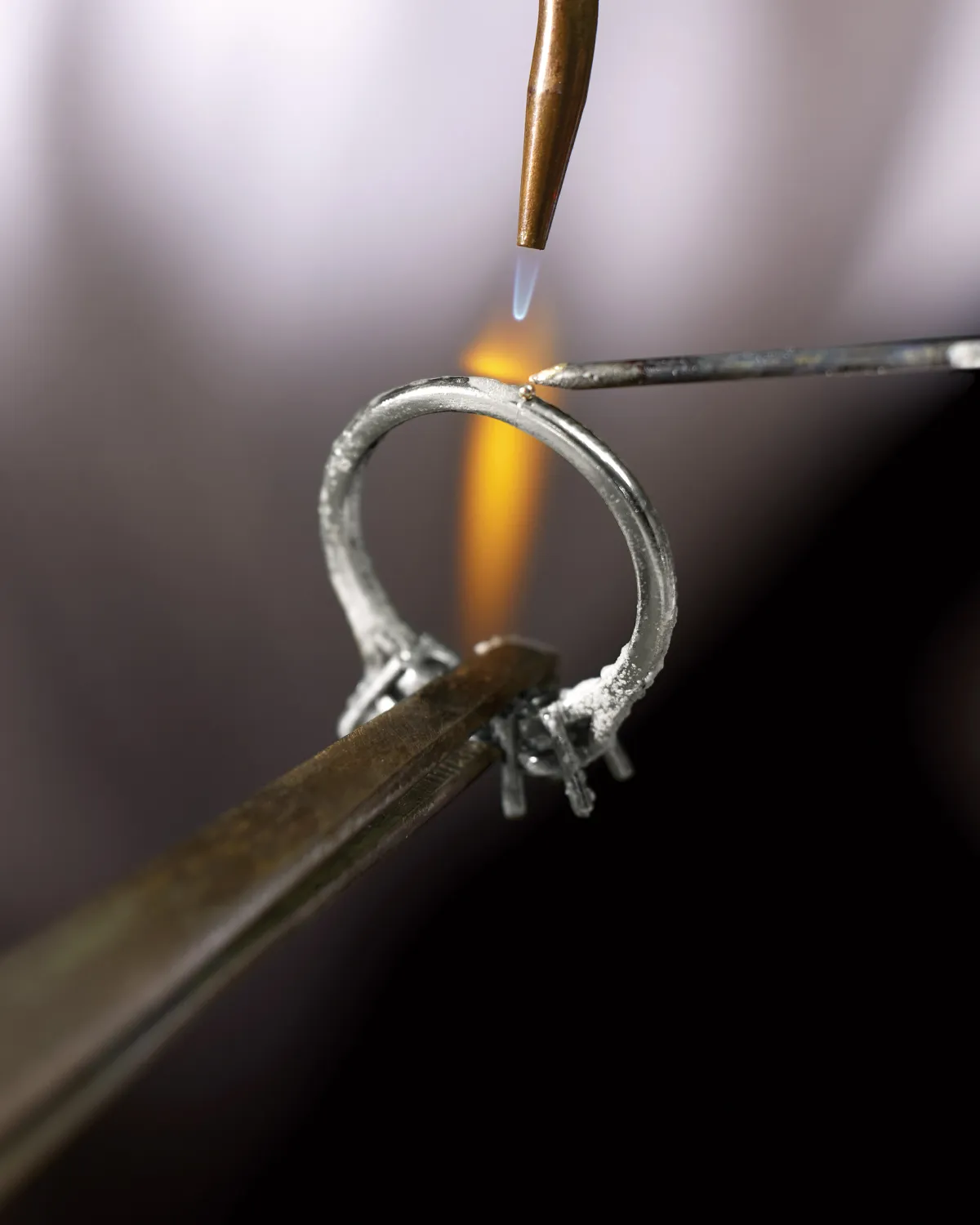Jeweler soldering a ring with a flame and tools.